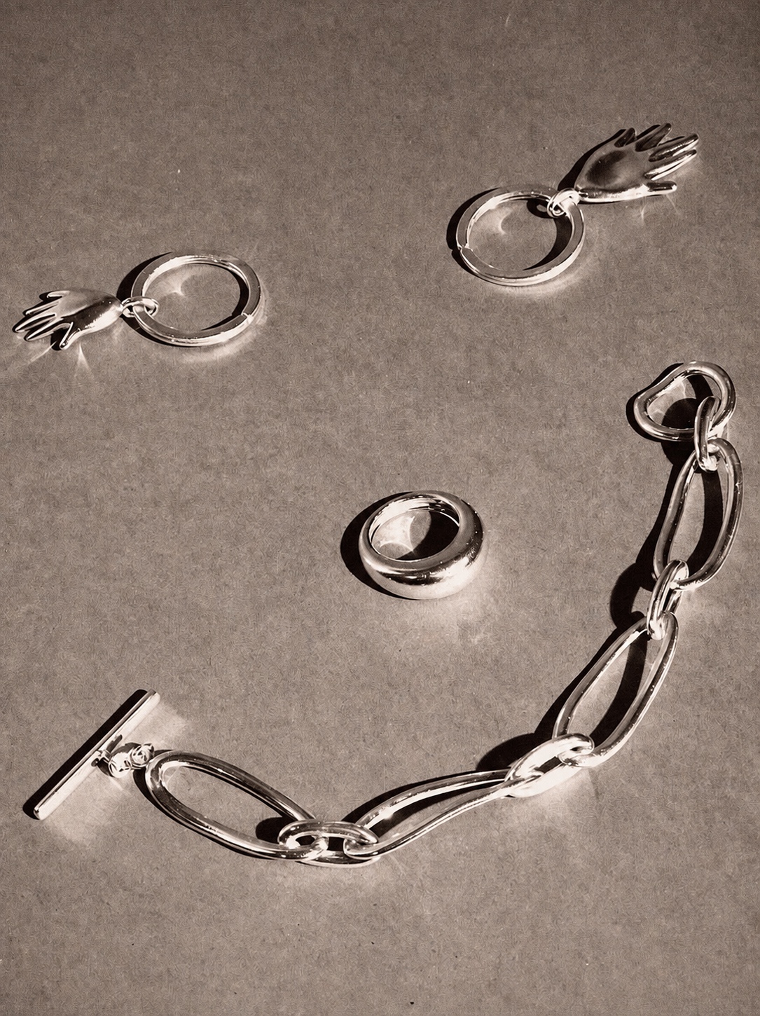 AGMES silver earrings and bracelet arranged on a textured surface