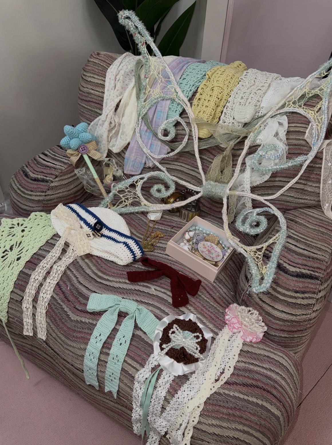 Openwork fairy wings, crochet hats, long ribbons and pastel accessories arranged across a striped armchair.