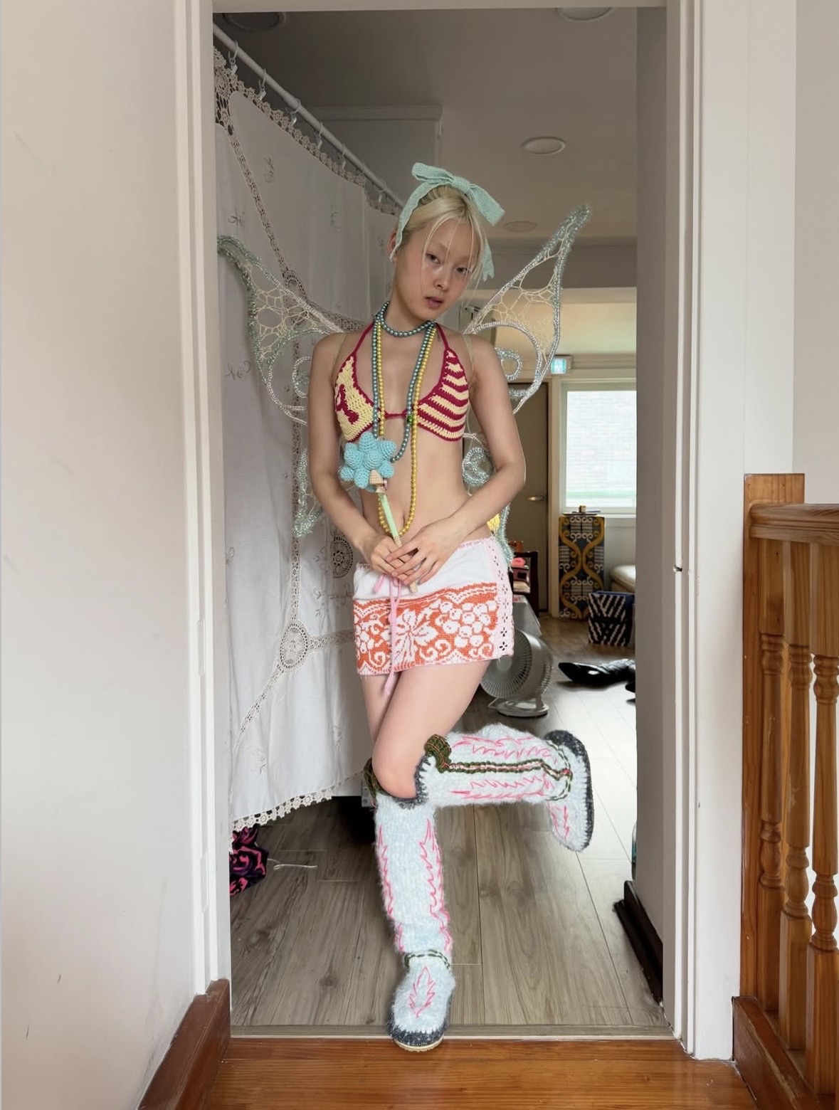 Full-body view of a model in fairy wings, a striped bikini top, patterned shorts and pale embellished boots.