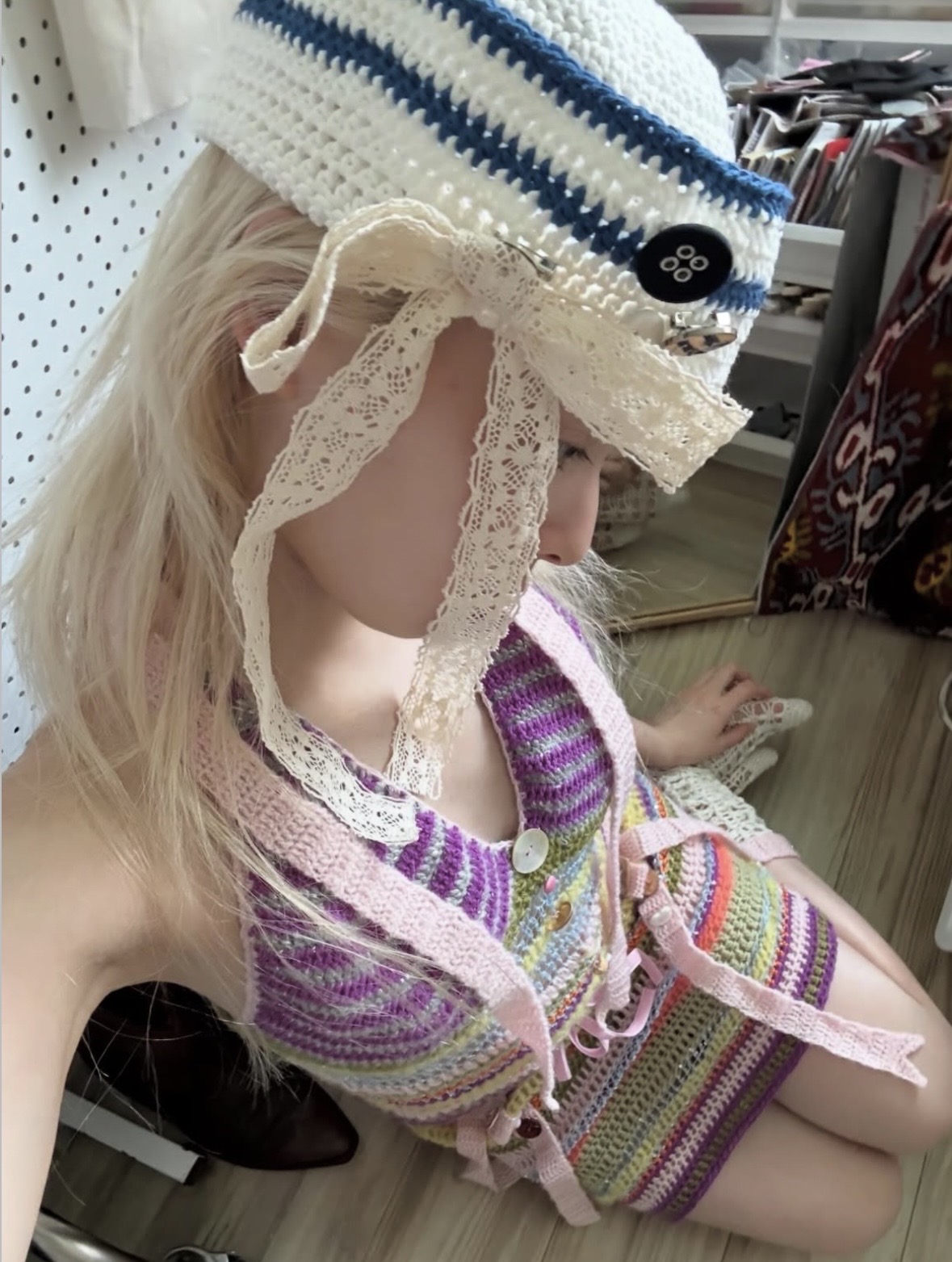 Overhead view of a striped crochet outfit with pink straps and decorative buttons, topped by a lace-trimmed sailor hat.