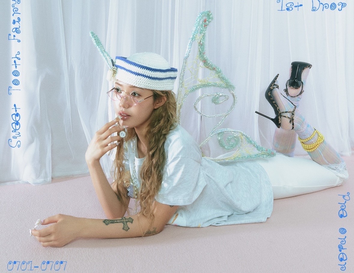 Editorial image of a model lying on her stomach in a pale blue outfit, sailor hat and fairy wings.