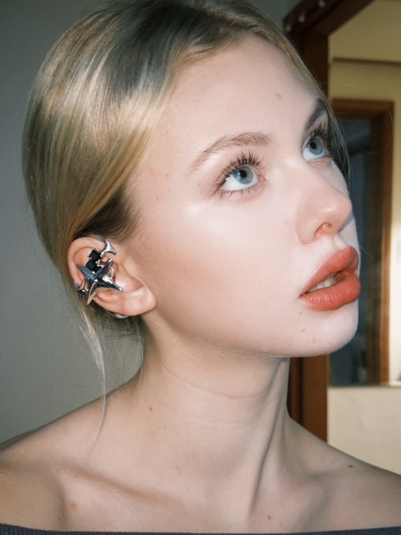 Side-profile portrait of a wearer in a grey knit top with a sculptural silver open earphone.