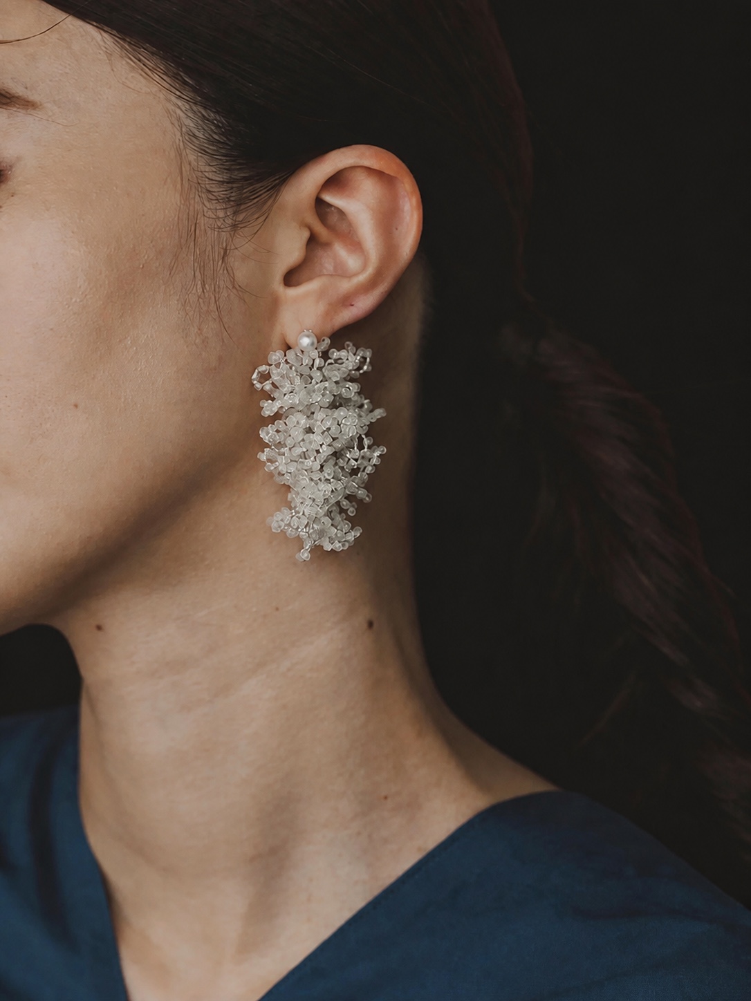 FUA white beaded statement earring against dark clothing