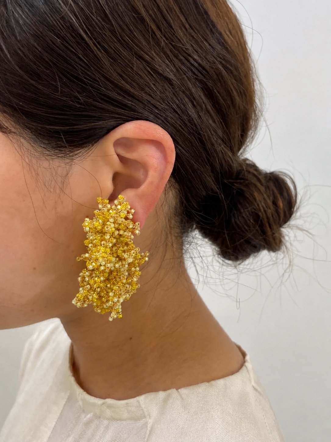 FUA yellow beaded earring worn with a white top