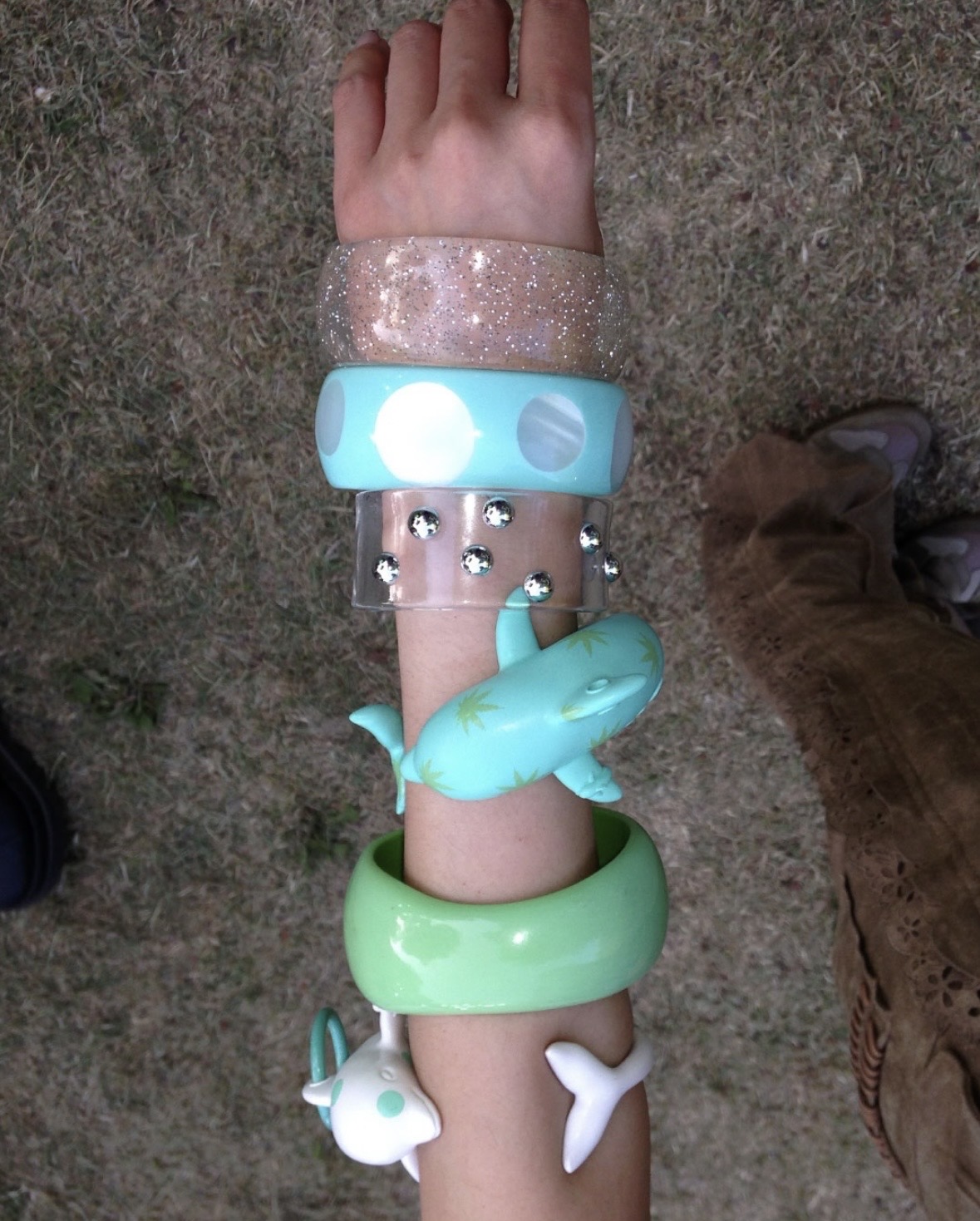 Overhead view of an arm stacked with glitter, turquoise, clear and green bangles, including dolphin-shaped cuffs.