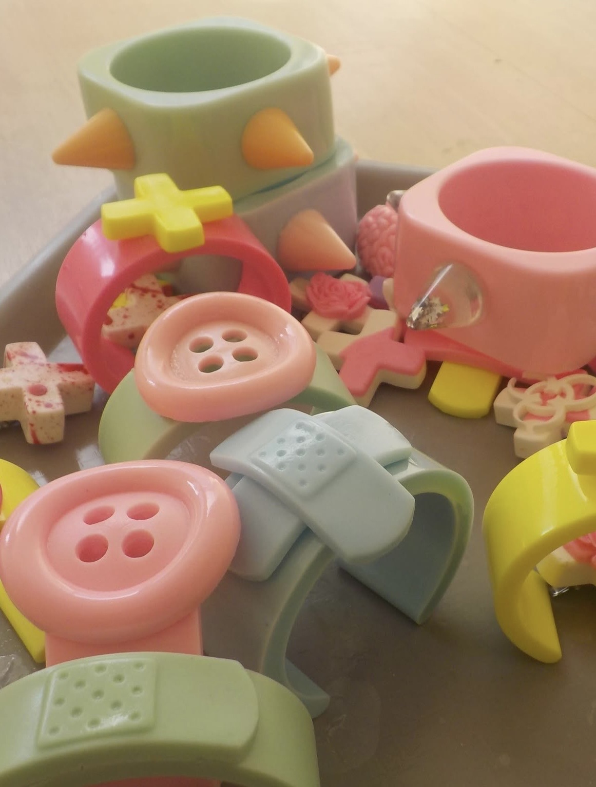 Pile of pastel chunky cuffs decorated with oversized buttons, bandage shapes, crosses and pointed studs.