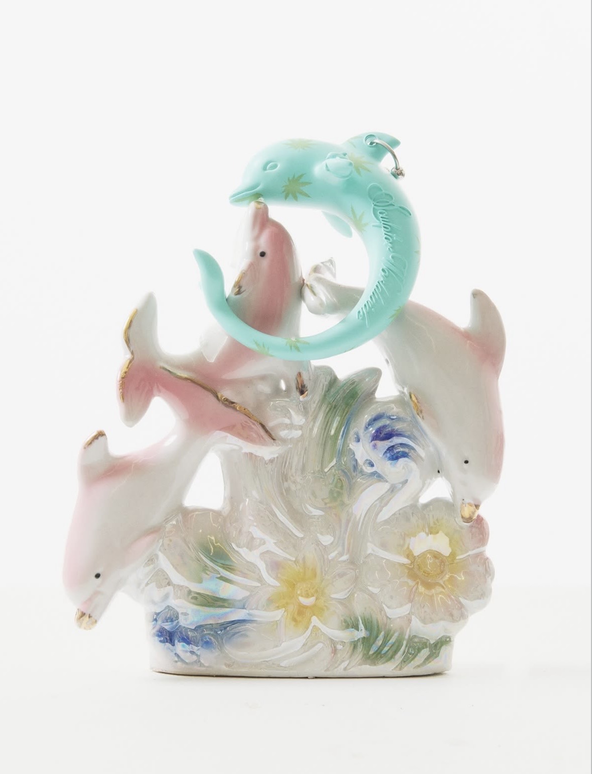 Turquoise dolphin-shaped bracelet displayed on a glossy ornament of dolphins leaping above waves and flowers.