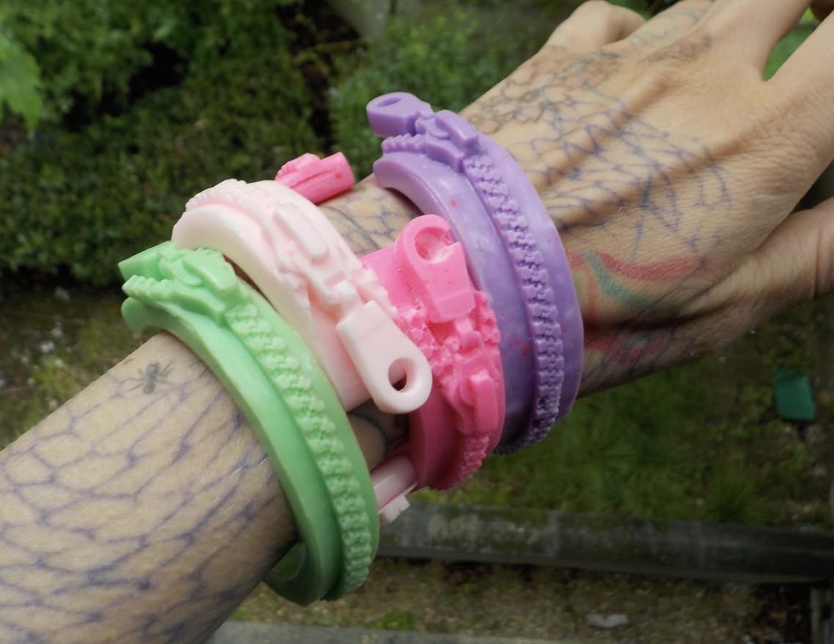 Close-up of green, white, pink and purple zipper-shaped bracelets stacked on a tattooed forearm.