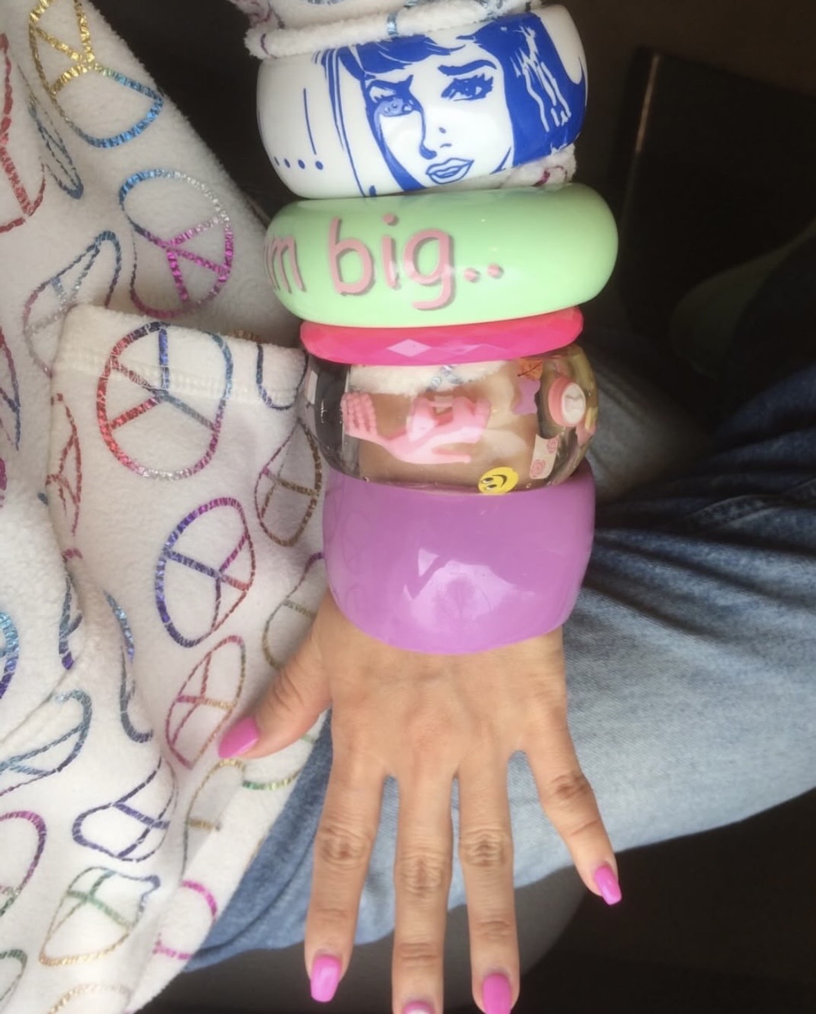 Arm stacked with purple, green, pink and clear bangles beside a cream top printed with peace symbols.