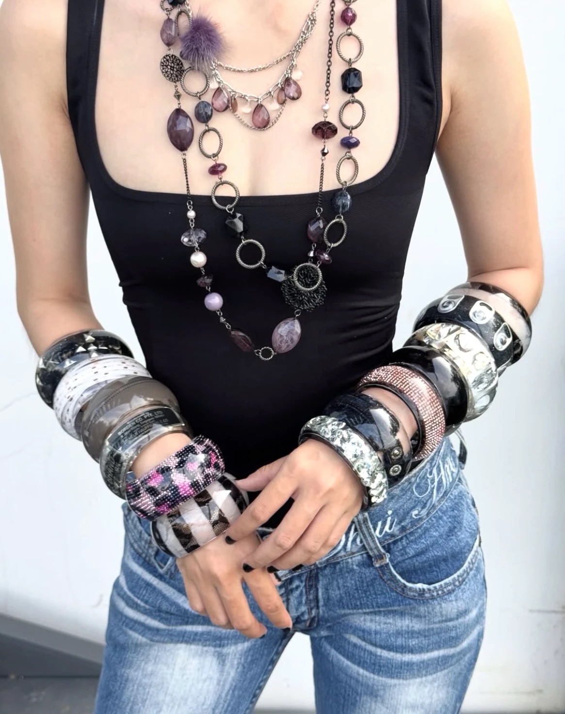 Black tank top and jeans styled with long purple necklaces and mixed black, white and silver-colored wrist stacks.