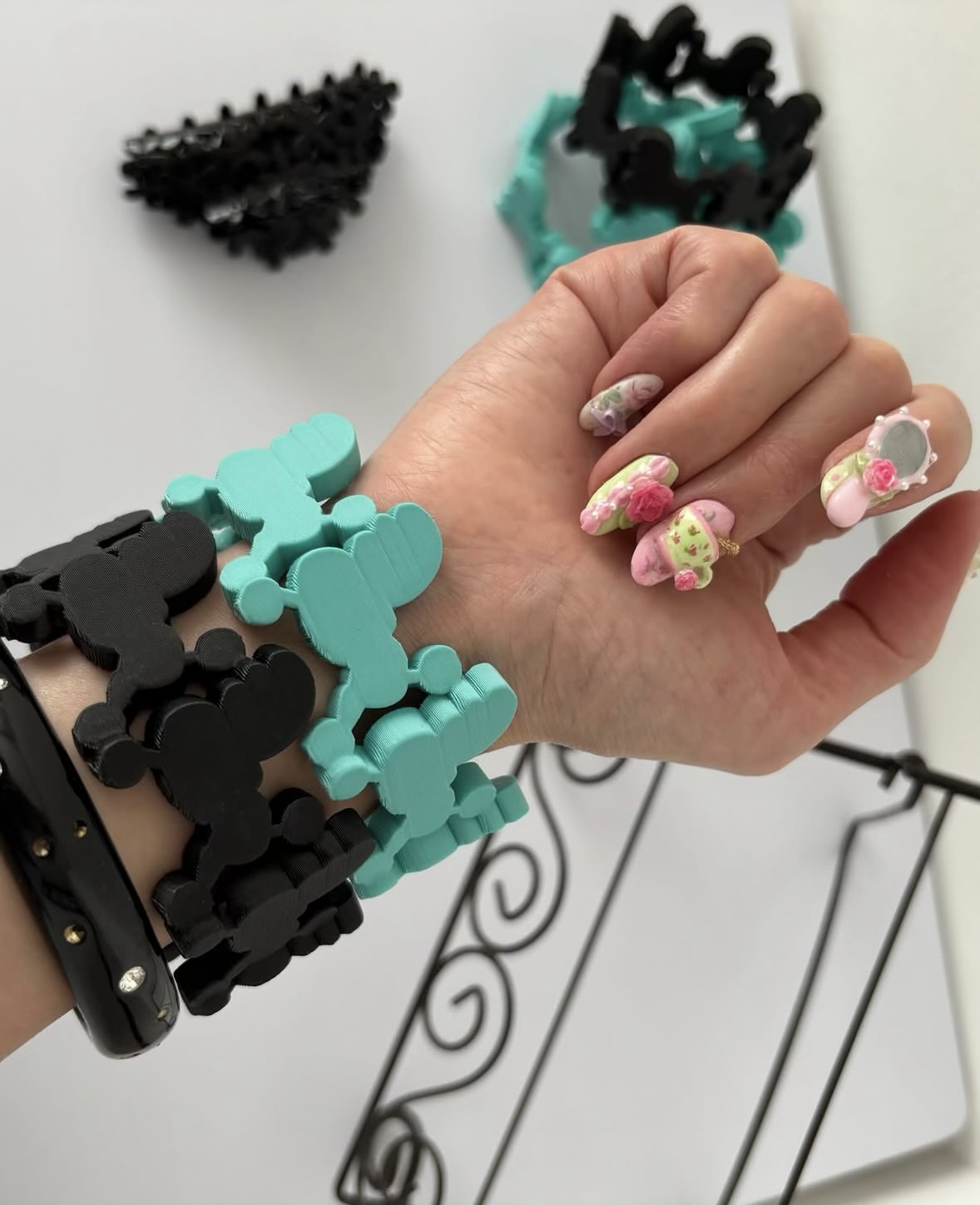 Black and turquoise bear-shaped link bracelets beside miniature floral tea-set nail decorations.