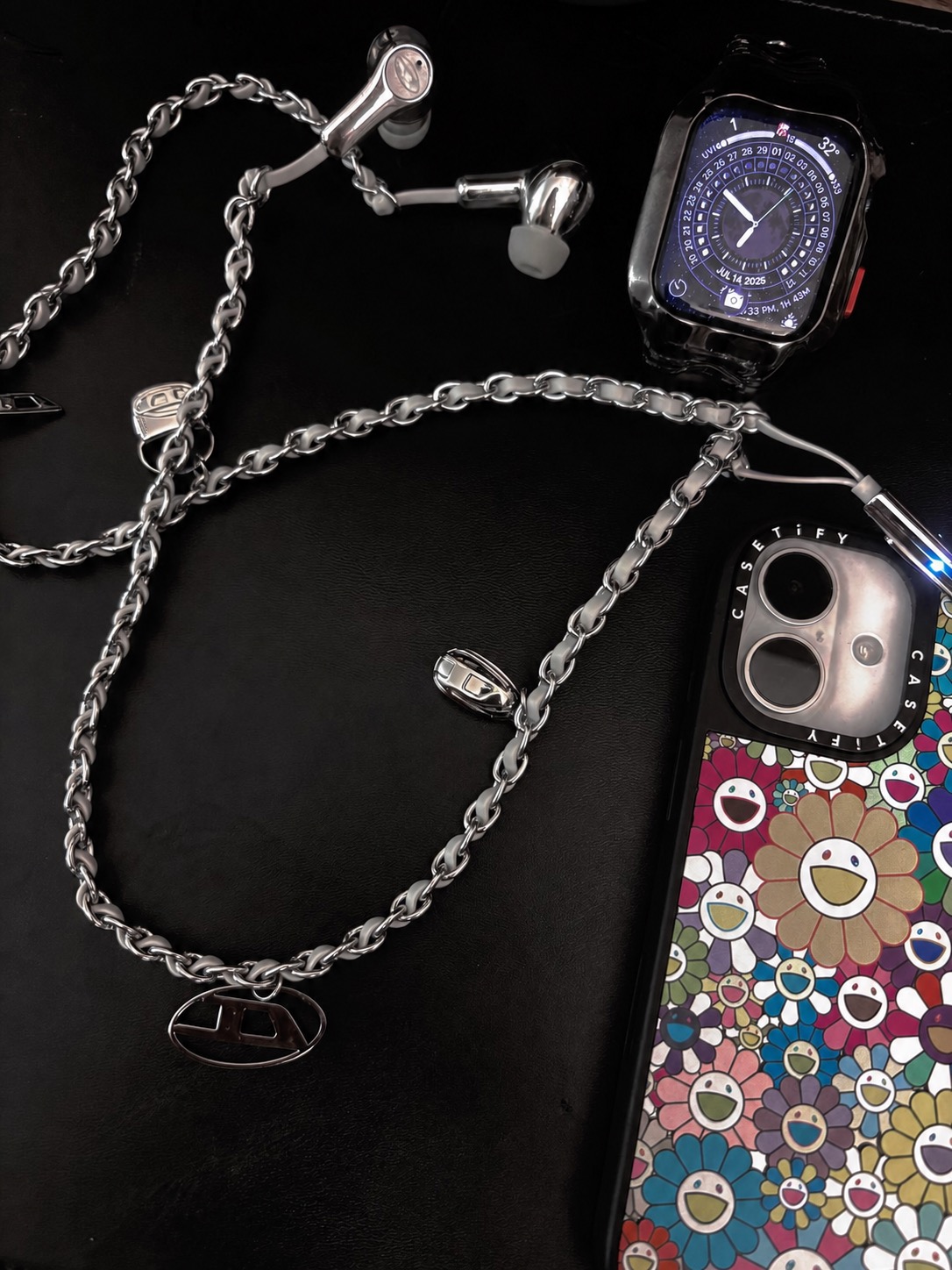 Diesel wired headphones styled with a silver chain, watch, and printed phone case