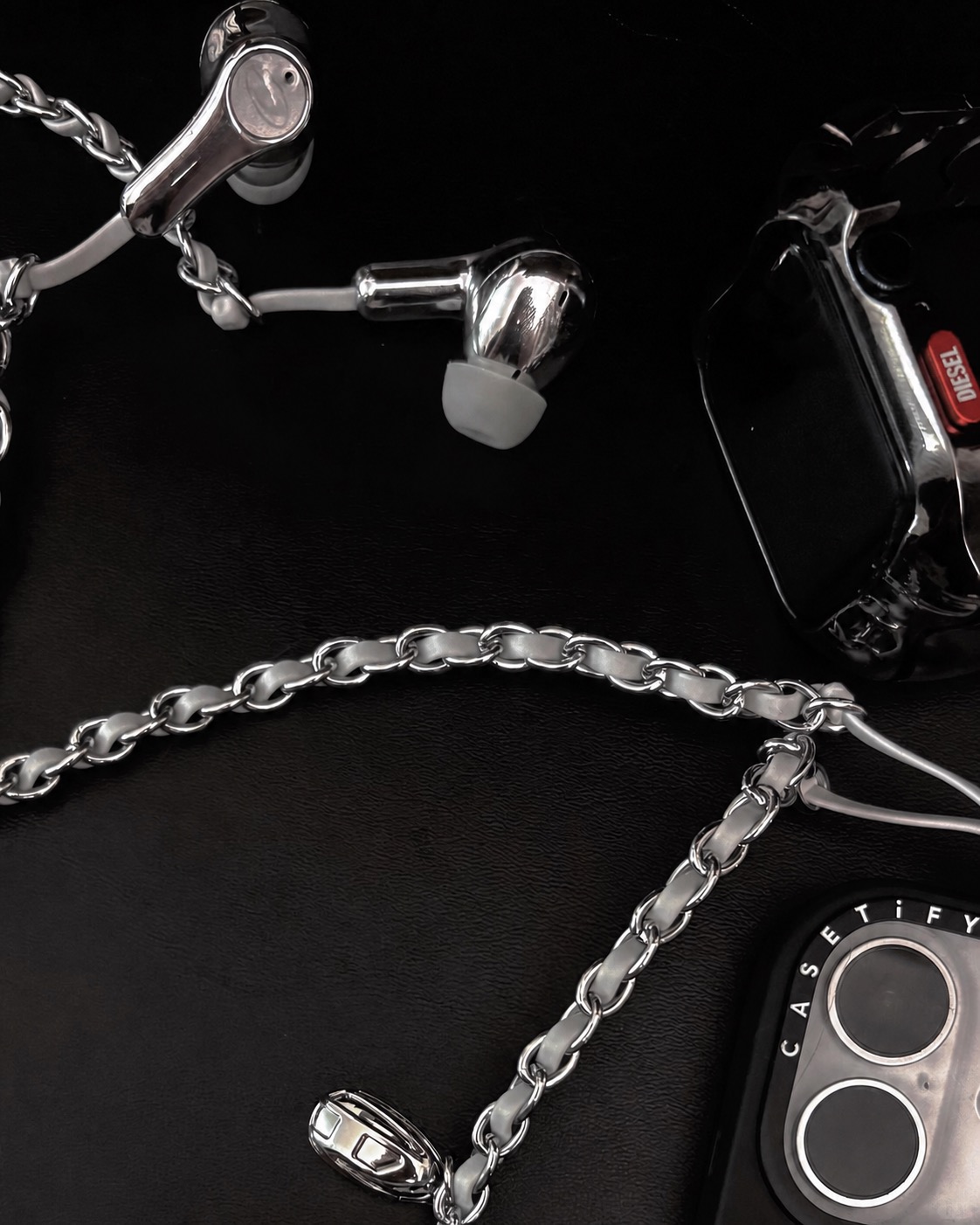 Close view of Diesel chain earphones with a black watch case and phone edge