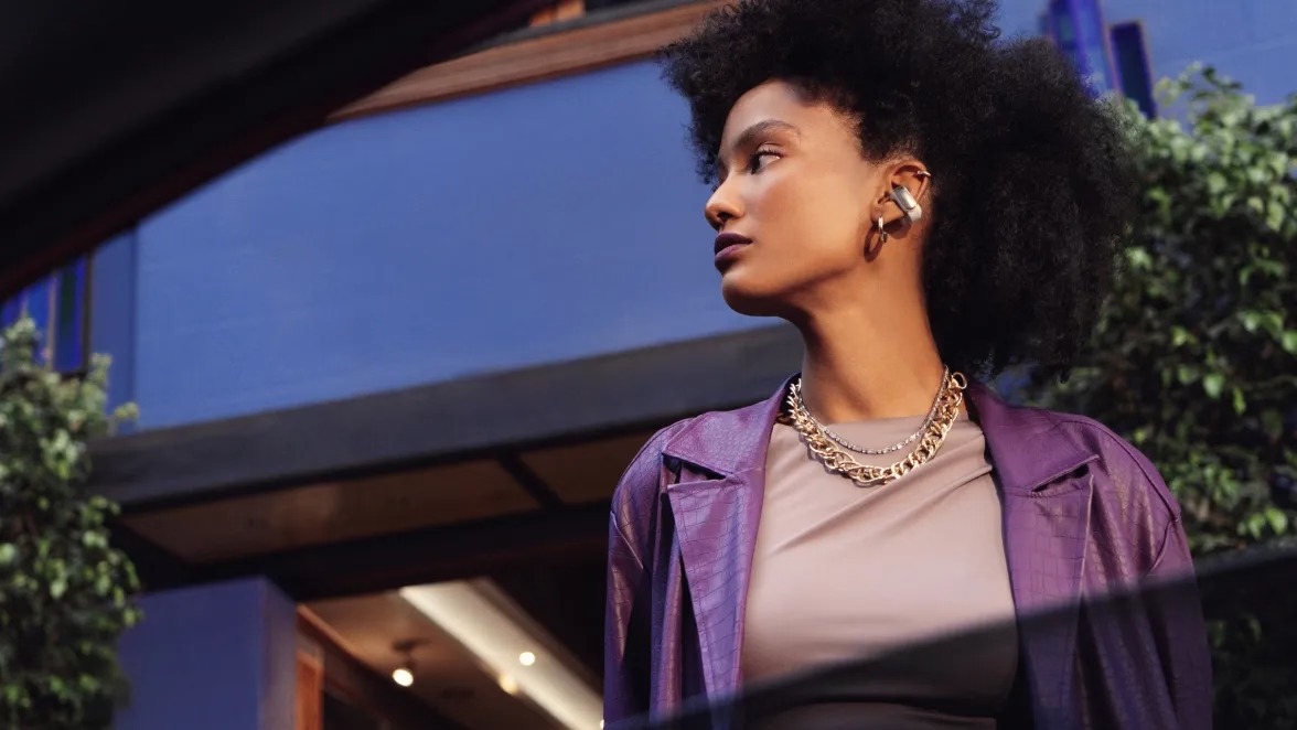 A person wearing Bose Ultra Open Earbuds with hoop earrings and a purple jacket outdoors.