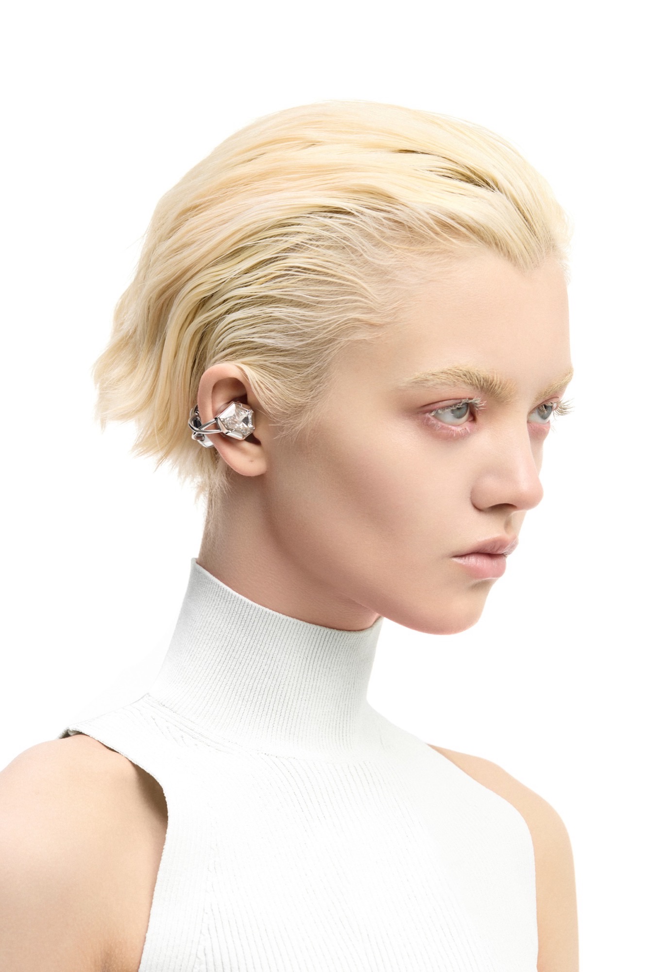 A model wearing silver OF HUNGER Electronic Gems with a clear faceted stone and a white sleeveless turtleneck.