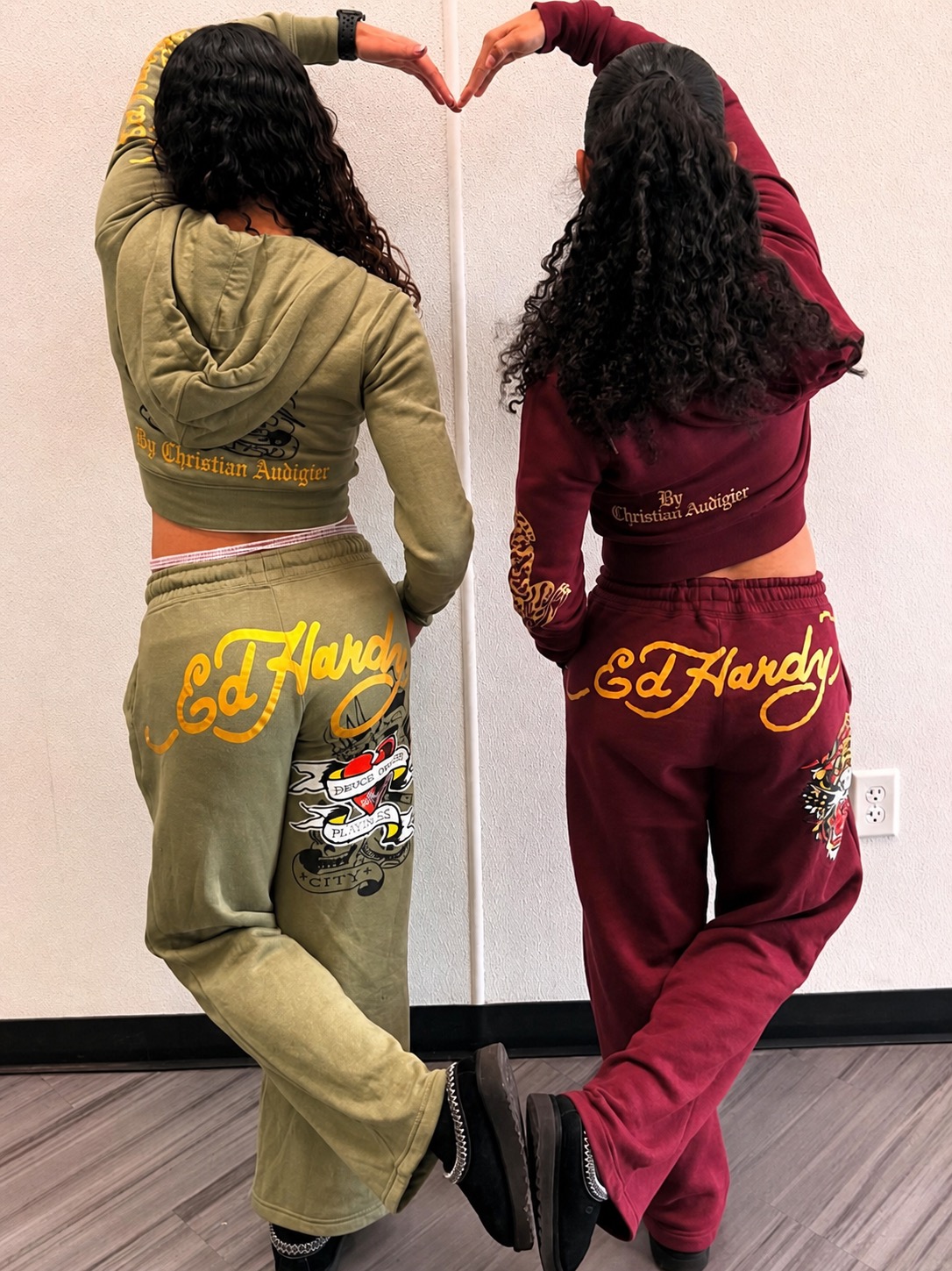 Two matching Ed Hardy tracksuits from the back, one olive and one burgundy, forming a heart with their hands.
