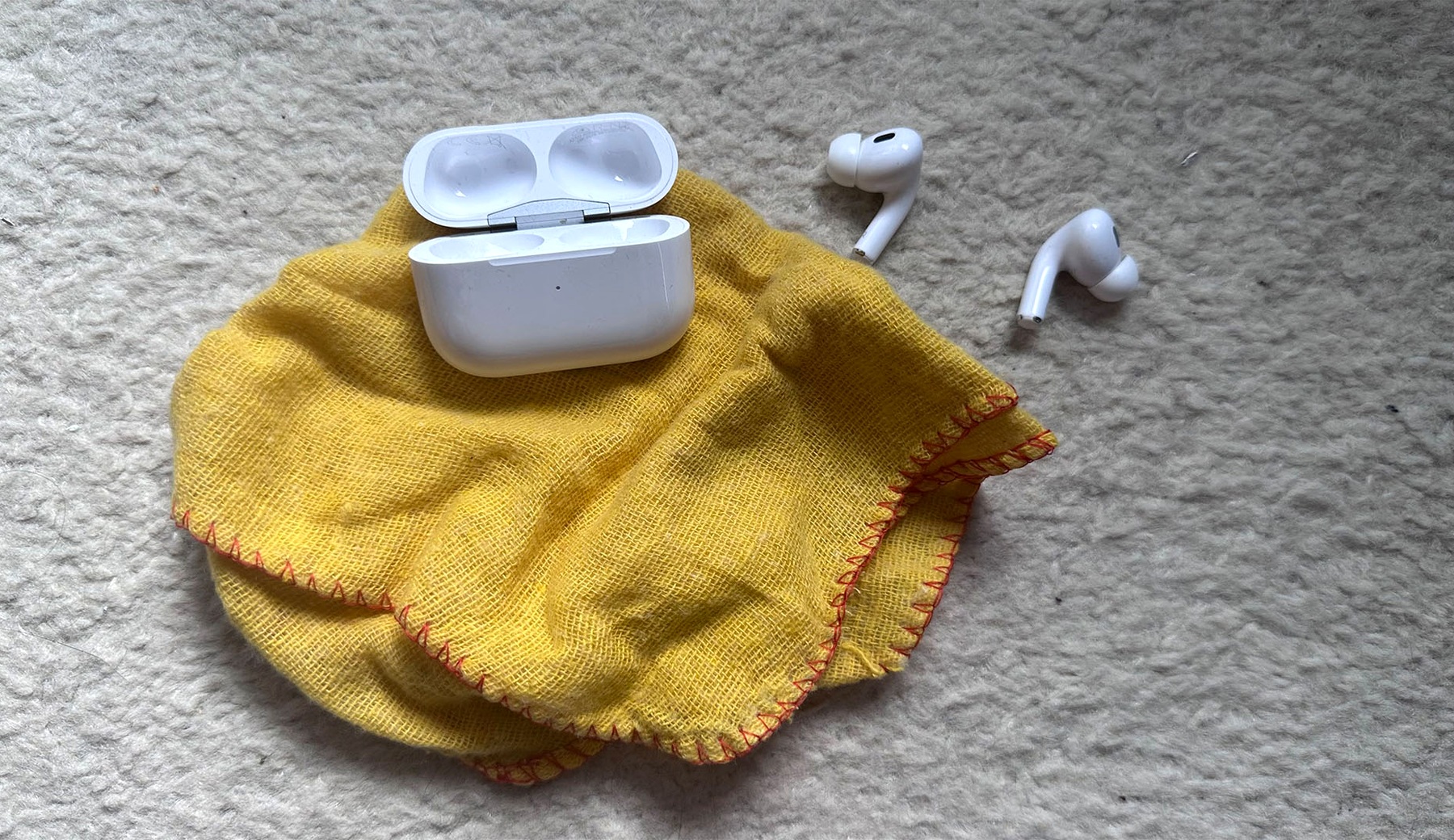 A fashion tech accessory's daily kit: earphone, charging case, cleaning cloth.