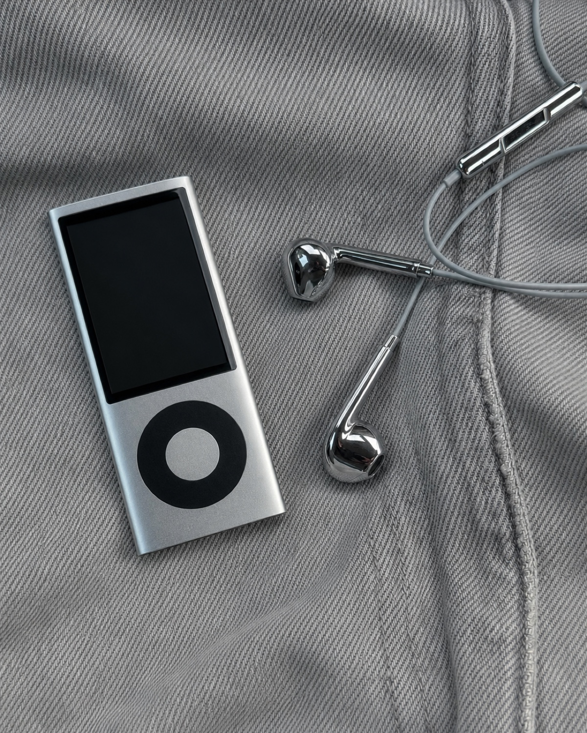 Mirror-chrome wired earbuds beside an unbranded silver music player on grey denim