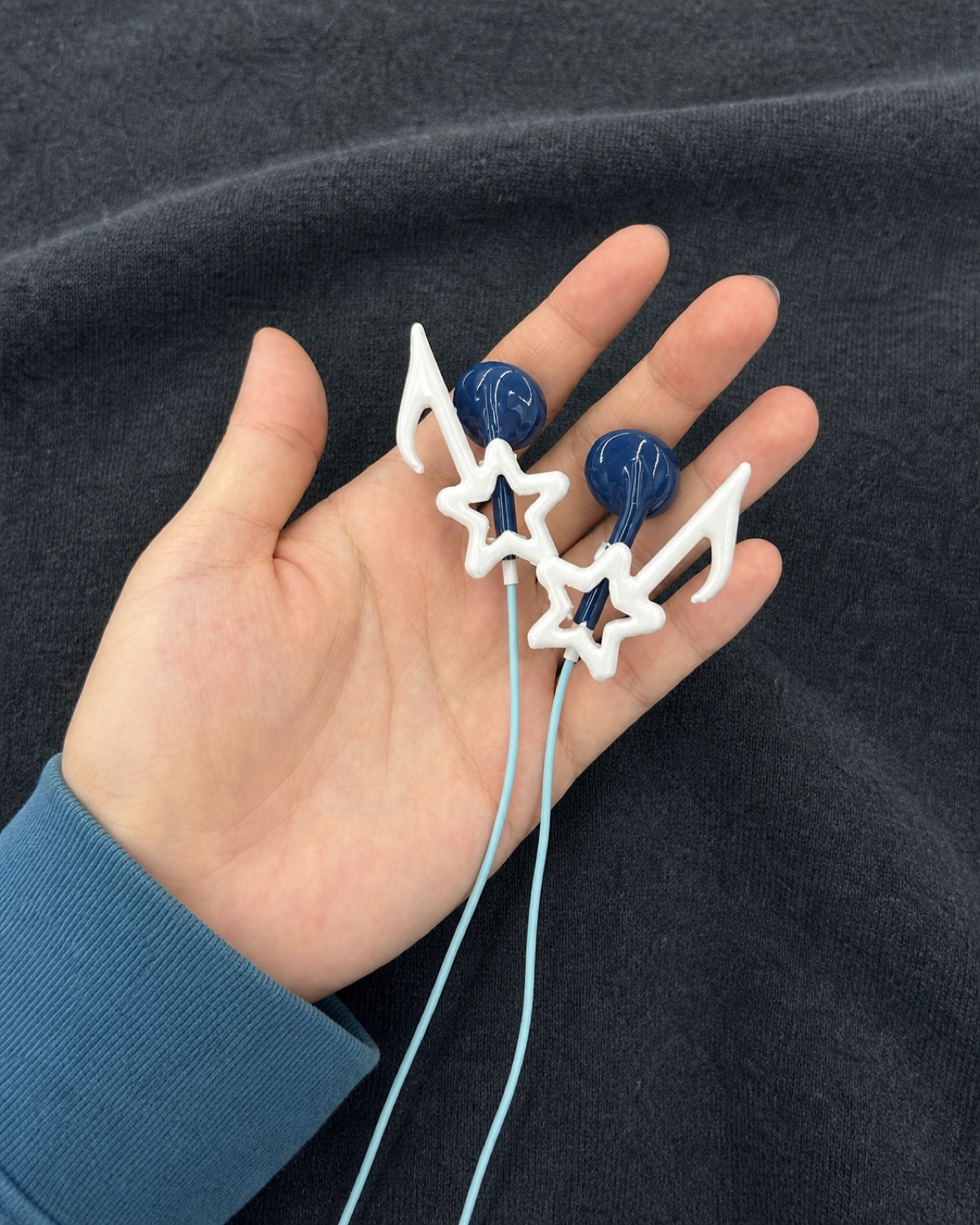 Hand holding navy wired earbuds with white star-shaped frames and pale-blue cables