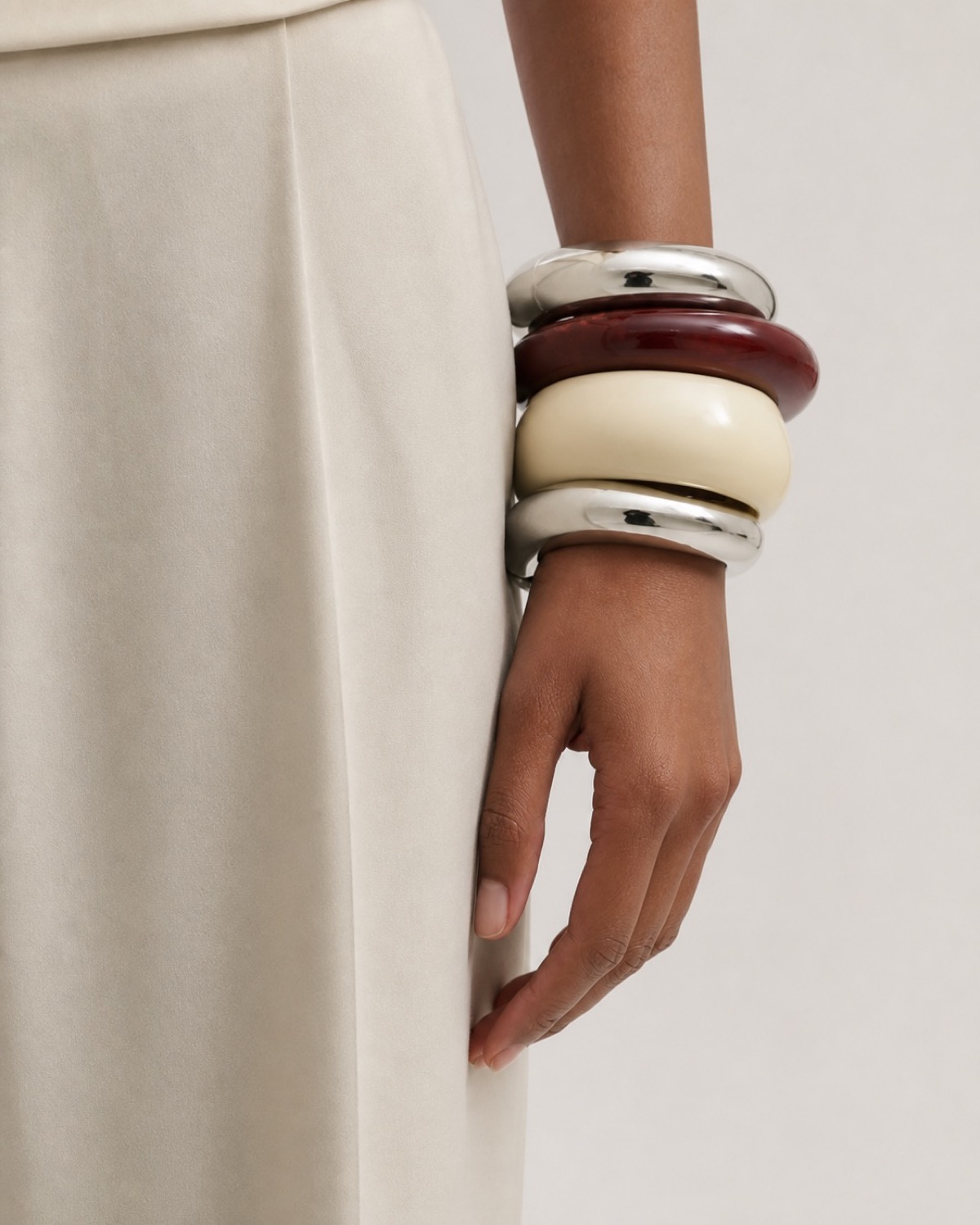 Four oversized bangles in silver, burgundy and ivory stacked beside a cream garment