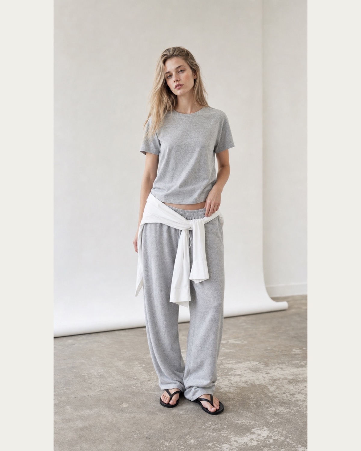 White shirt tied low around the waist over a grey T-shirt and loose sweatpants