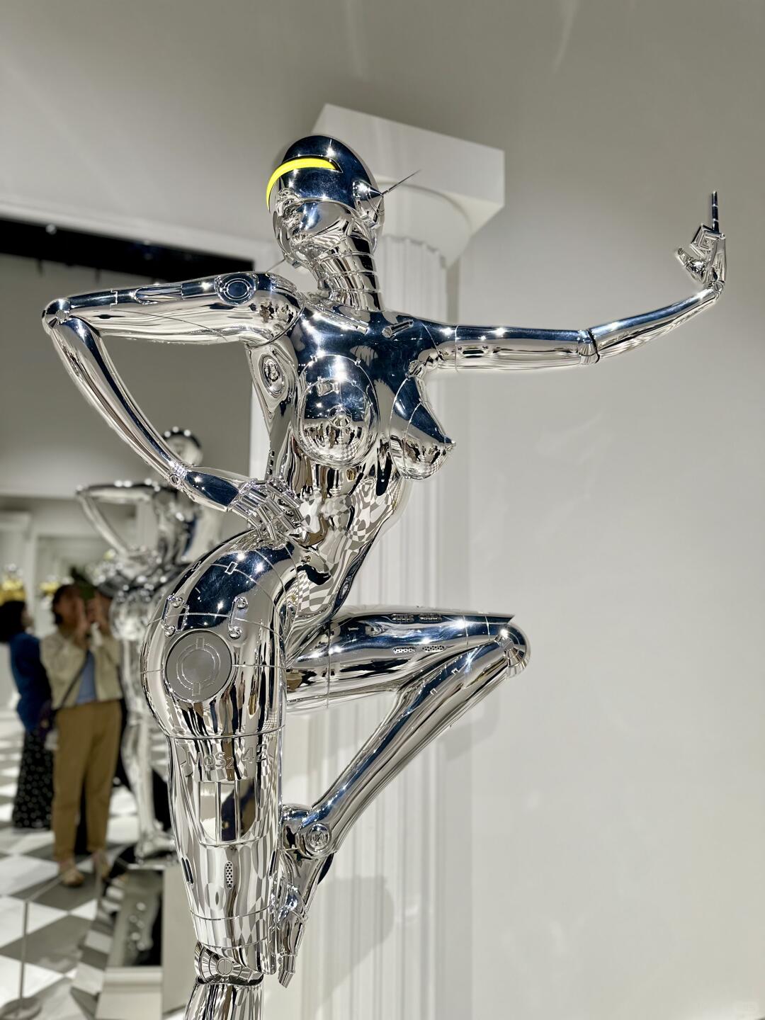 Chrome robot posing with one leg raised in white gallery space
