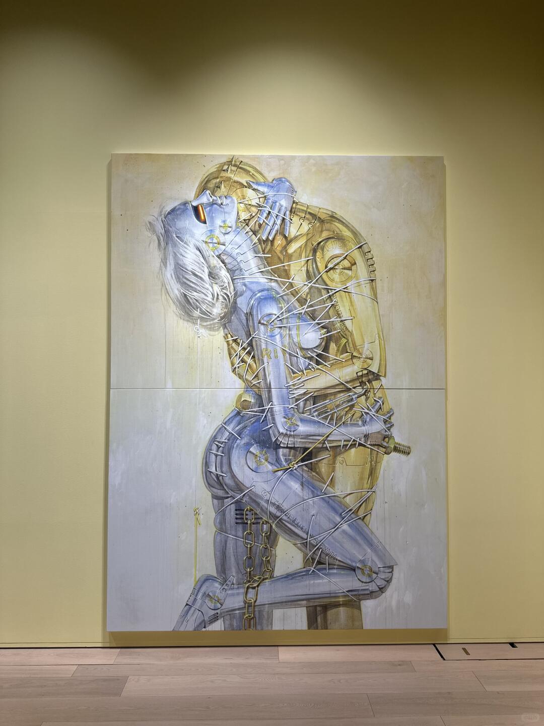 Large painting of chrome robot body folded in a warm exhibition room