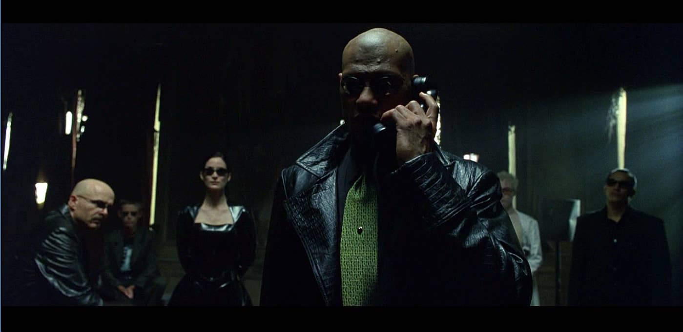 Morpheus in a textured black coat and sunglasses, with Trinity and other characters behind him in The Matrix.