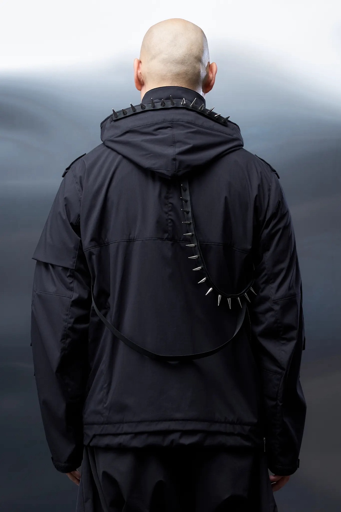 Back view of the black ACRONYM J1W-E jacket with metal-studded trim around the collar and across the back.