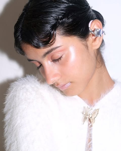 Side-lit close-up of a sculptural metallic ear piece worn against pulled-back hair.