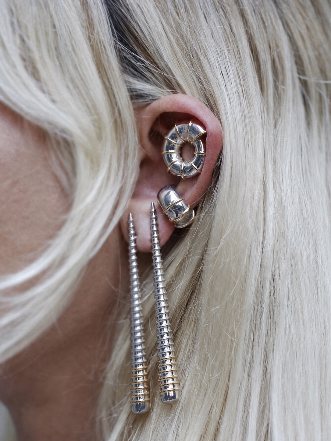 Silver and gold Jaagravii ear cuff earrings against pale hair