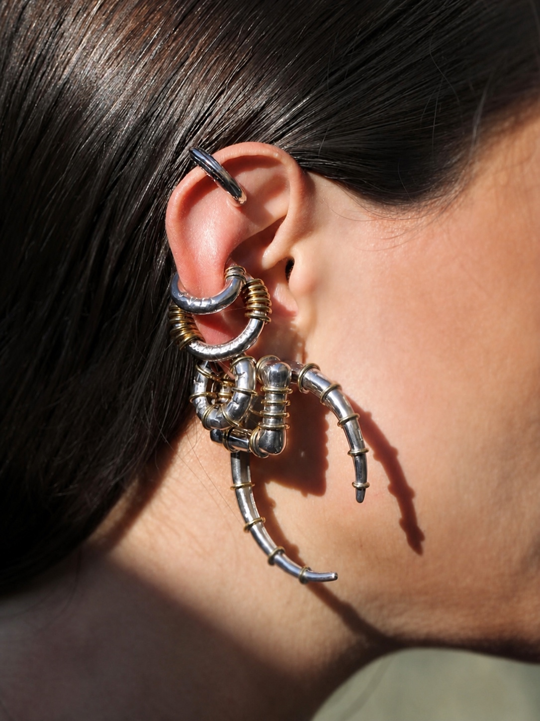 Layered silver and gold Jaagravii earrings on an ear