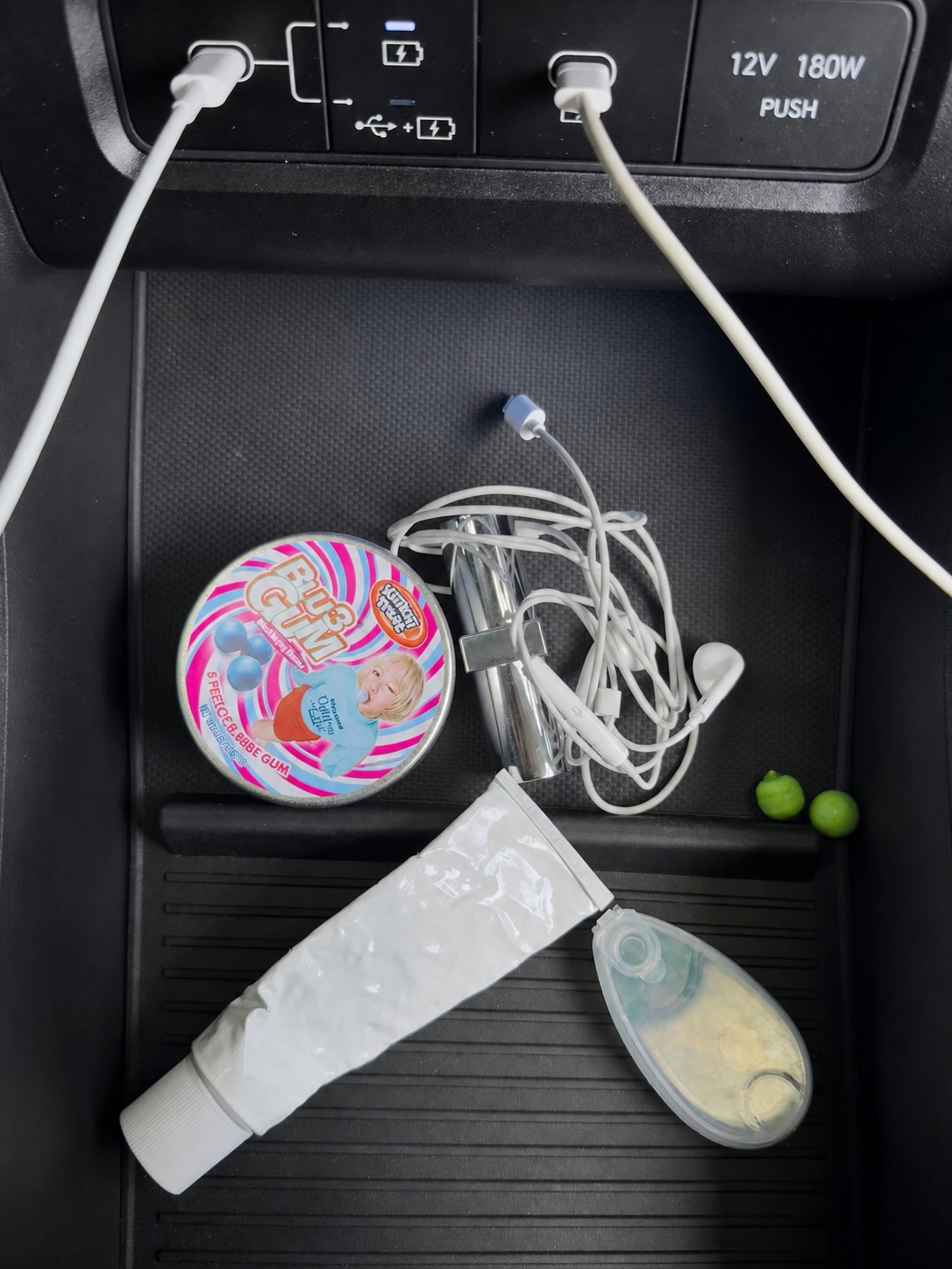 Bubble gum tin, wired earphones, and small objects in a car console