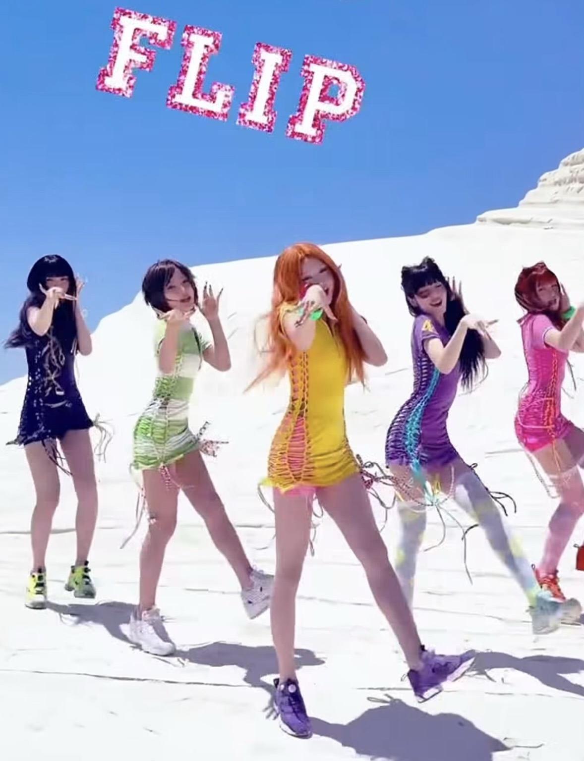 Five performers dancing in brightly colored lace-up mini dresses and chunky sneakers against a blue-and-white backdrop.