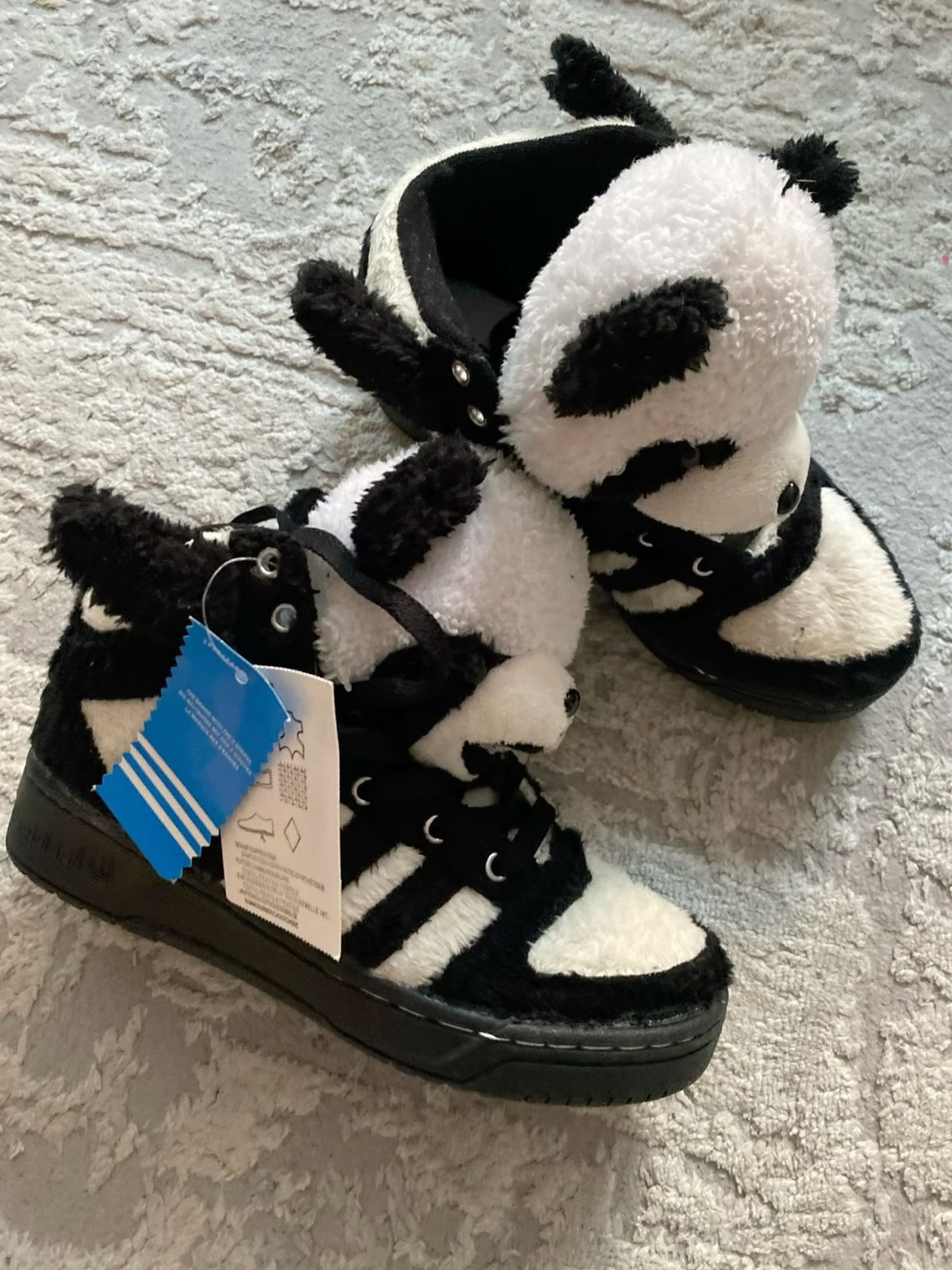 Black-and-white high-top sneakers with plush panda heads and arms attached around the tongues.