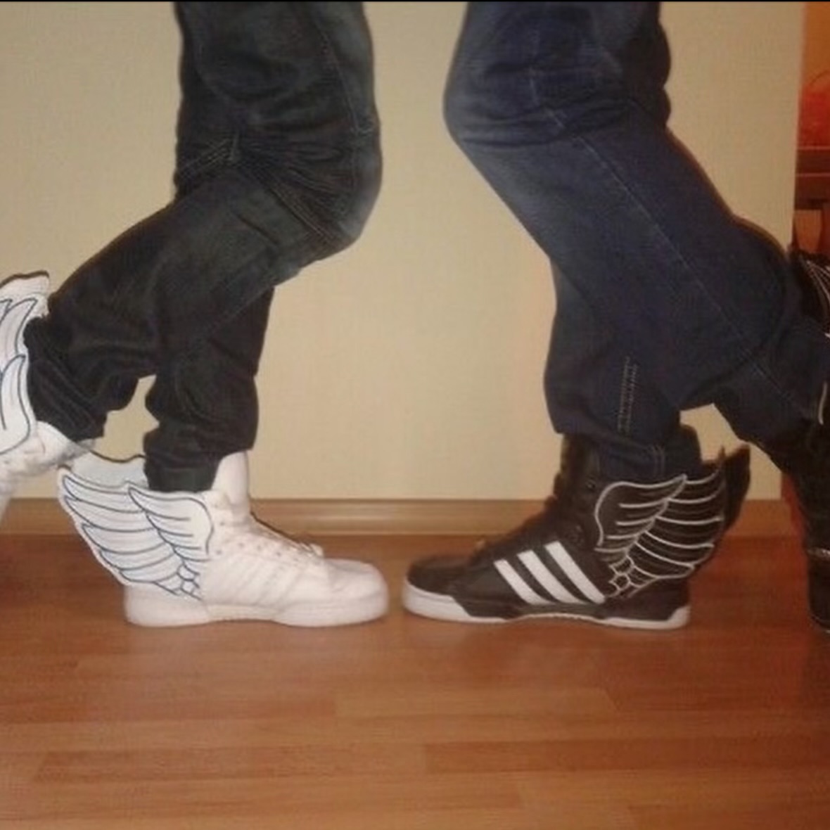 White and black adidas winged high-tops worn with dark skinny jeans on a wooden floor.
