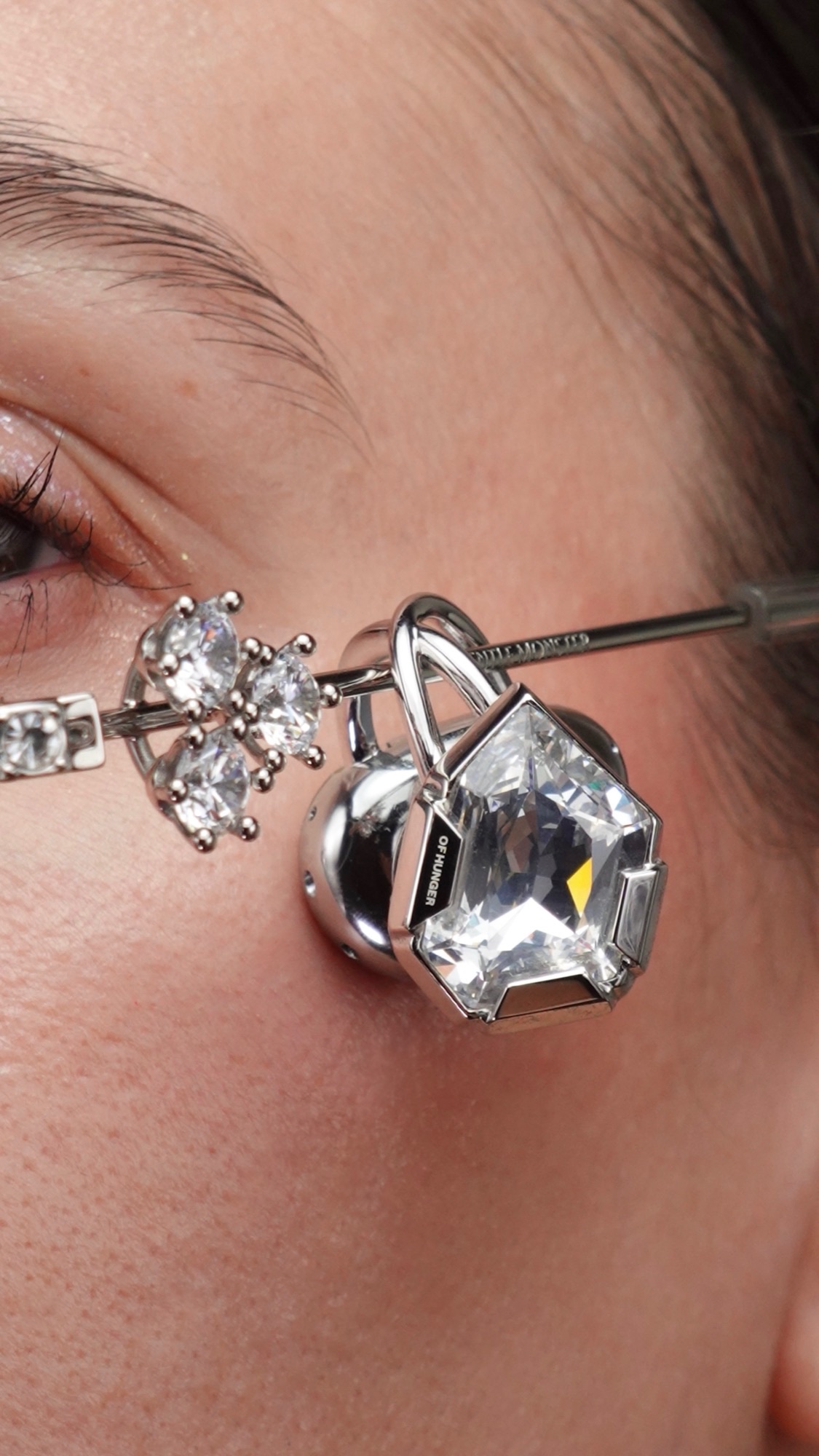 A silver case held in hand with faceted transparent gemstone ear pieces inside.