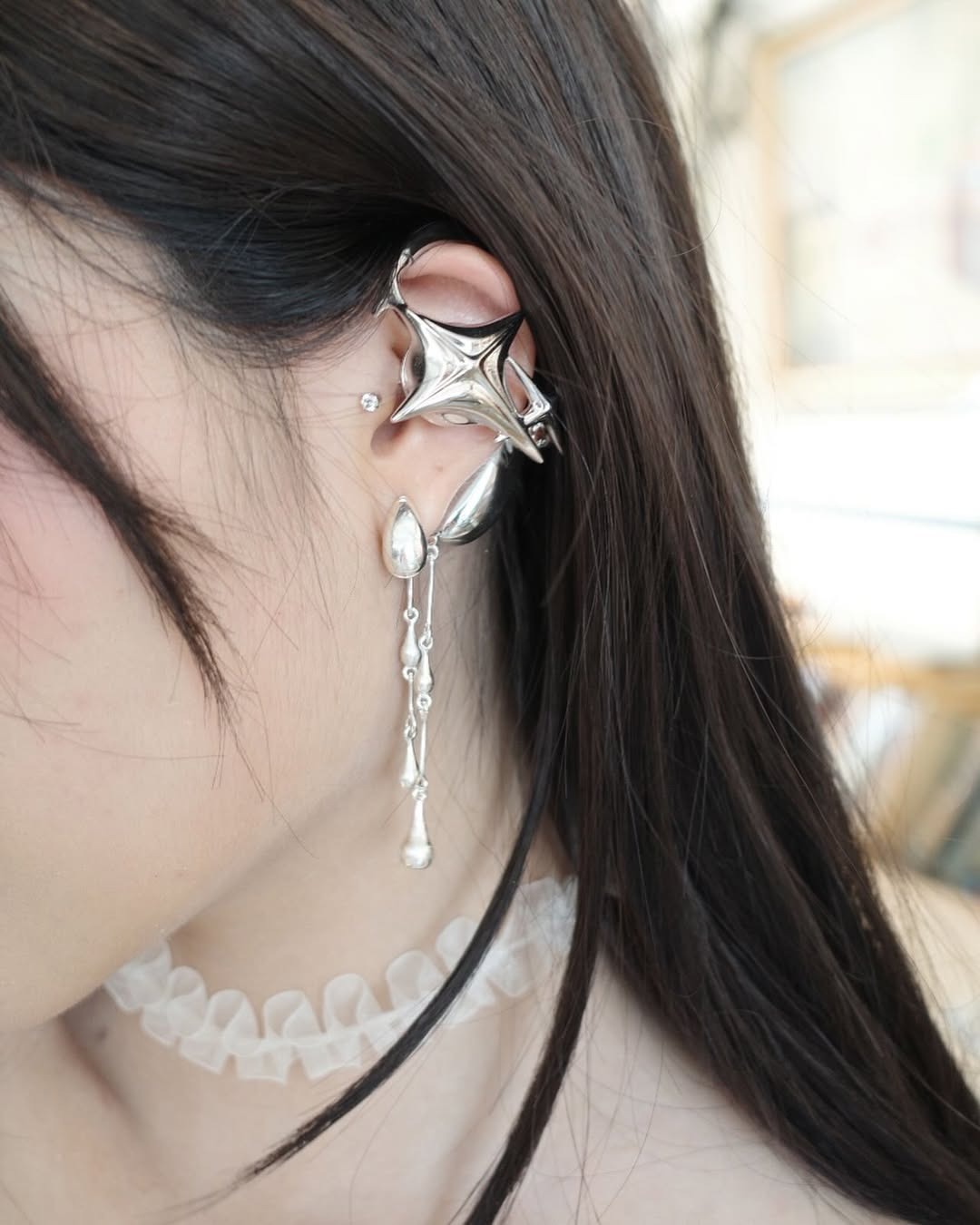 A hand holding silver sculptural open earphones above a branded gift box.