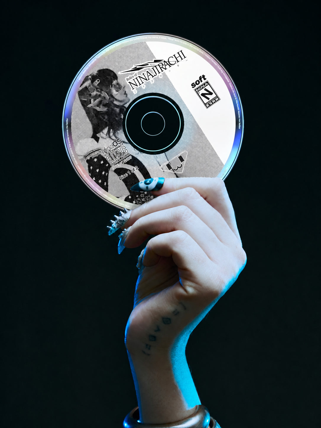 Hand holding a Ninajirachi CD with blue light and long decorated nails