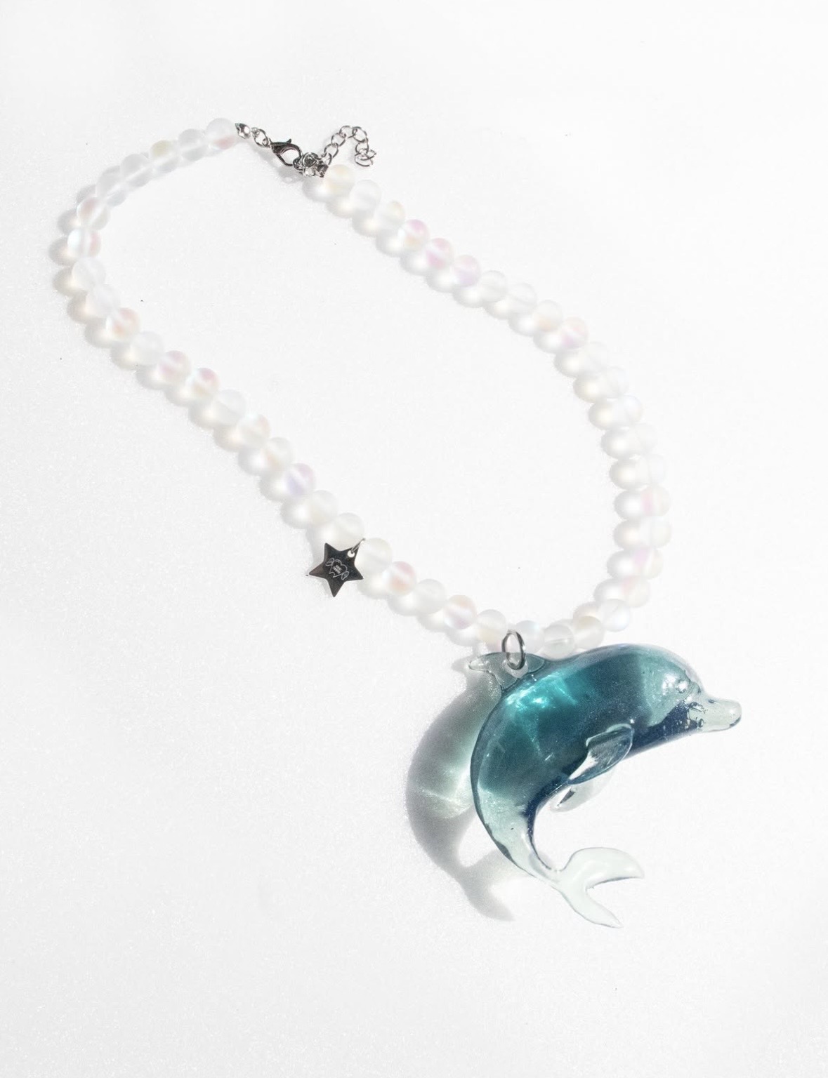 White bead necklace with a turquoise dolphin pendant and a small dark star, laid on a white background.