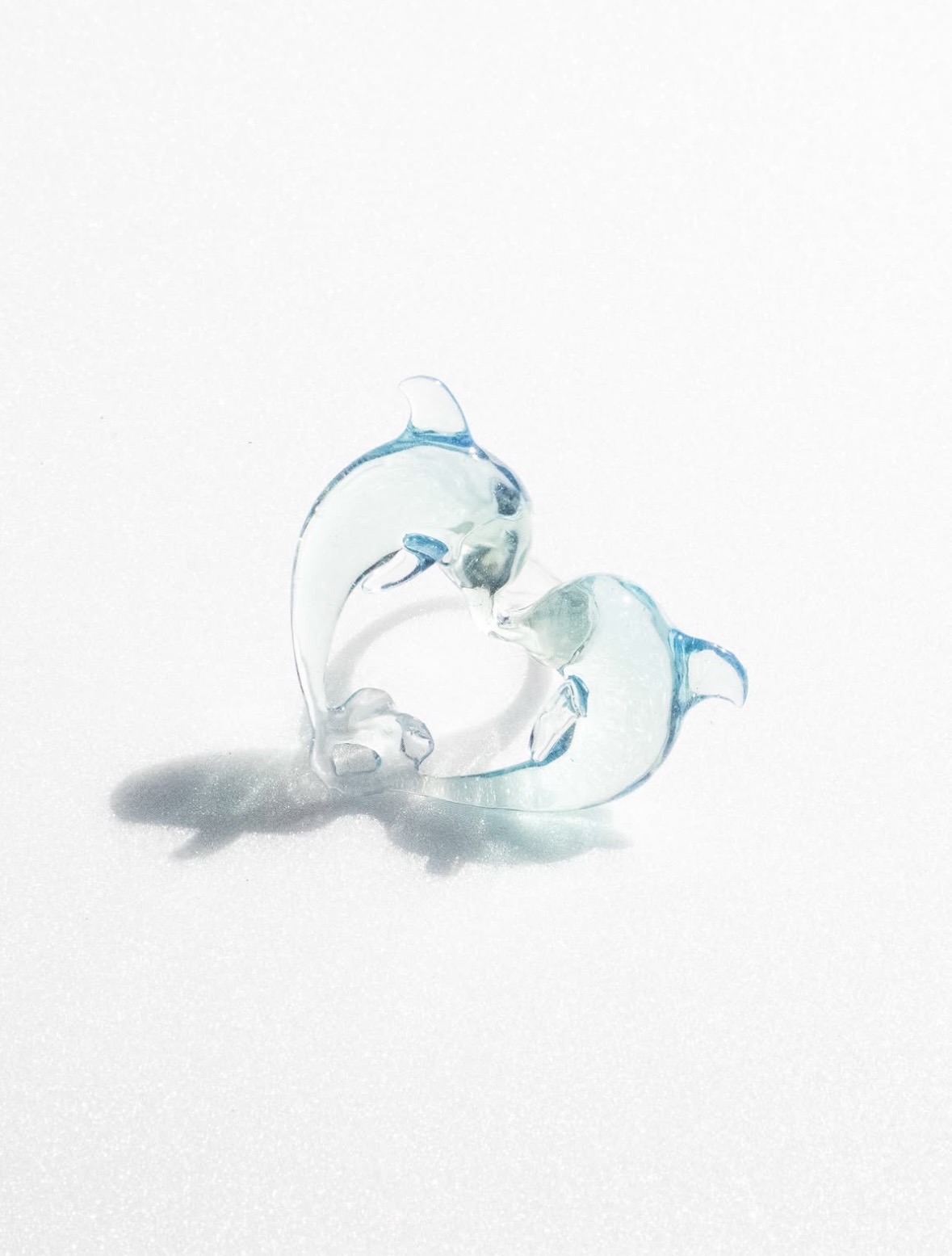 Two translucent blue dolphins forming a heart-shaped pendant on a white surface.