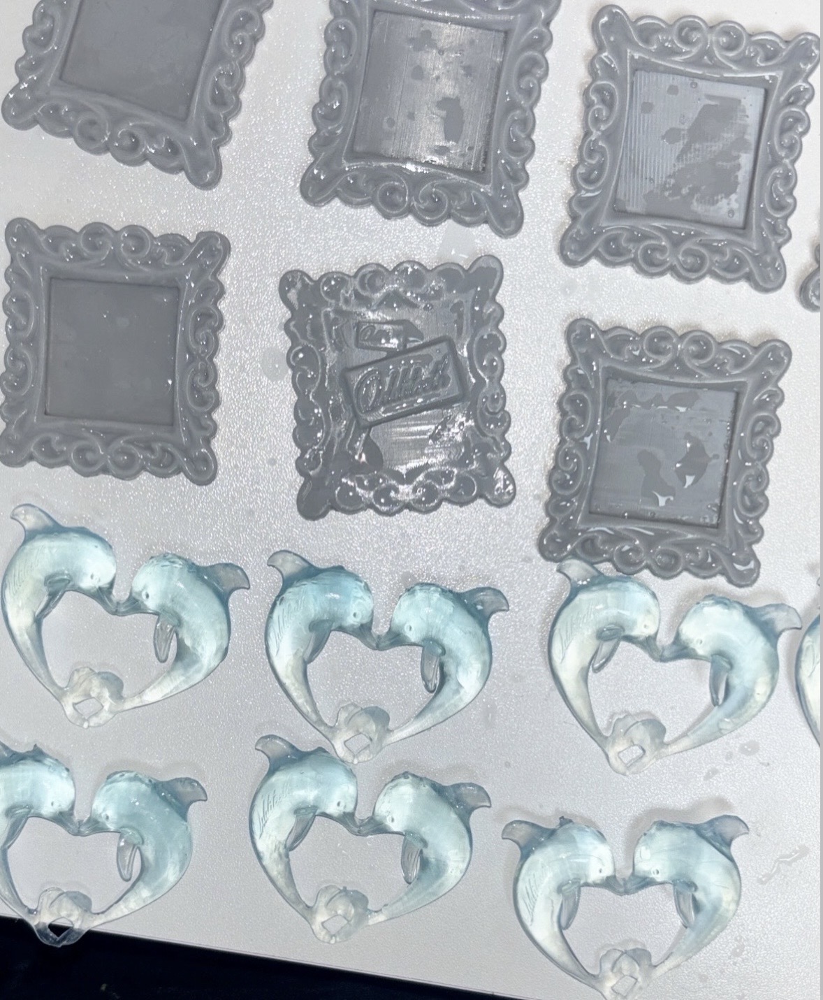Gray miniature picture frames and translucent dolphin-heart pendants arranged in rows on a work surface.