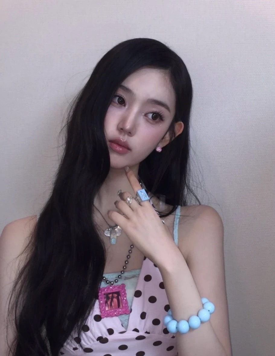 Dark-haired person in a pink polka-dot top wearing a pink photo-frame necklace and large blue bead bracelet.