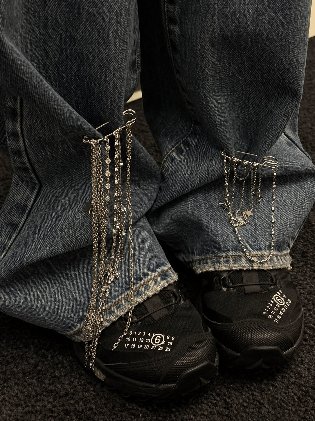 Silver trouser chains clipped to dark jeans over black technical sneakers