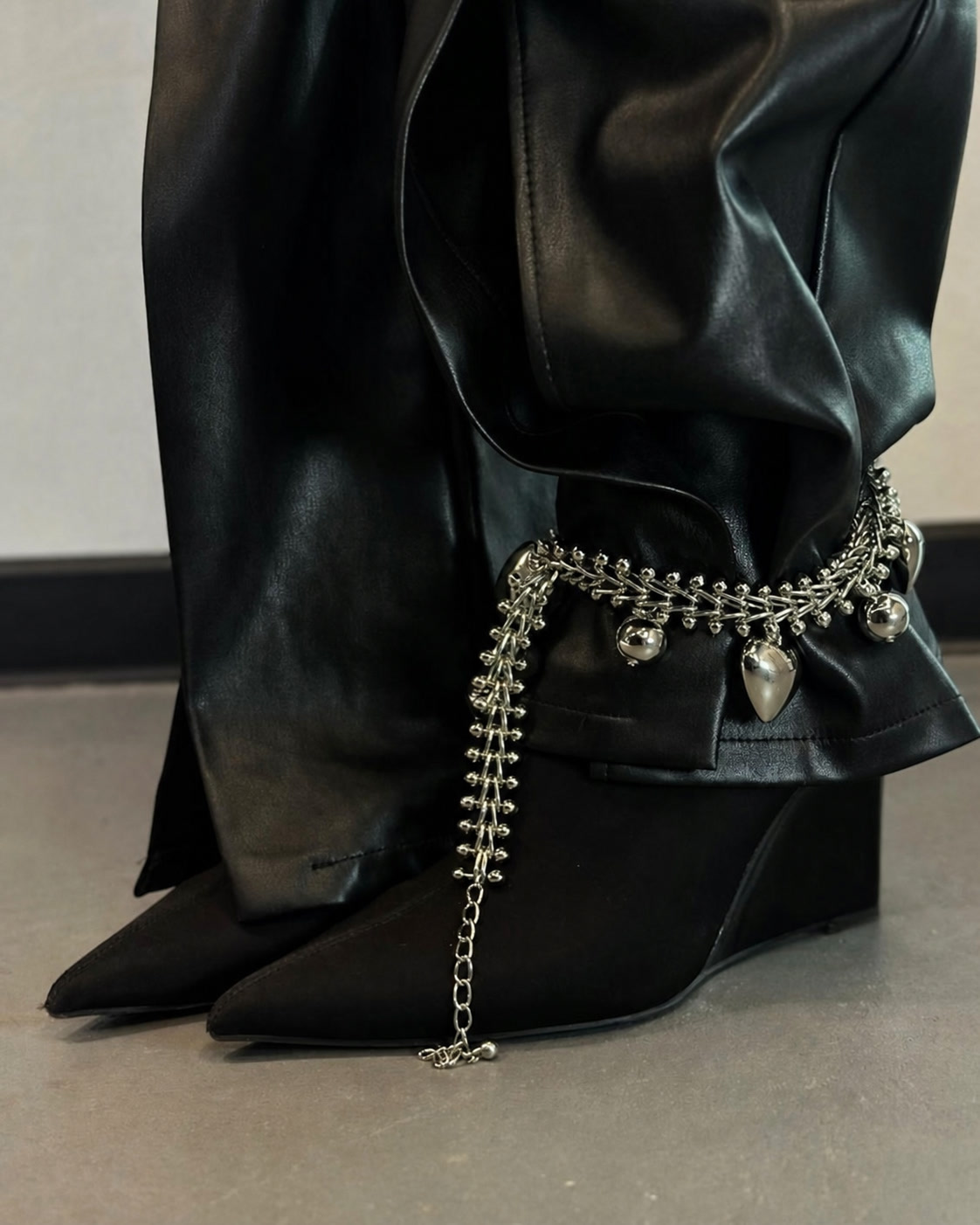 Silver chain jewelry wrapped around black leather trousers and pointed shoes
