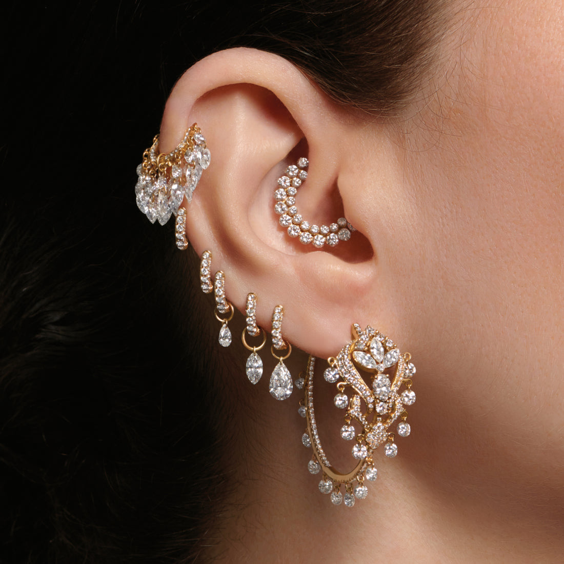 Maria Tash curated ear with layered gold and diamond earrings across the helix, conch, and lobe