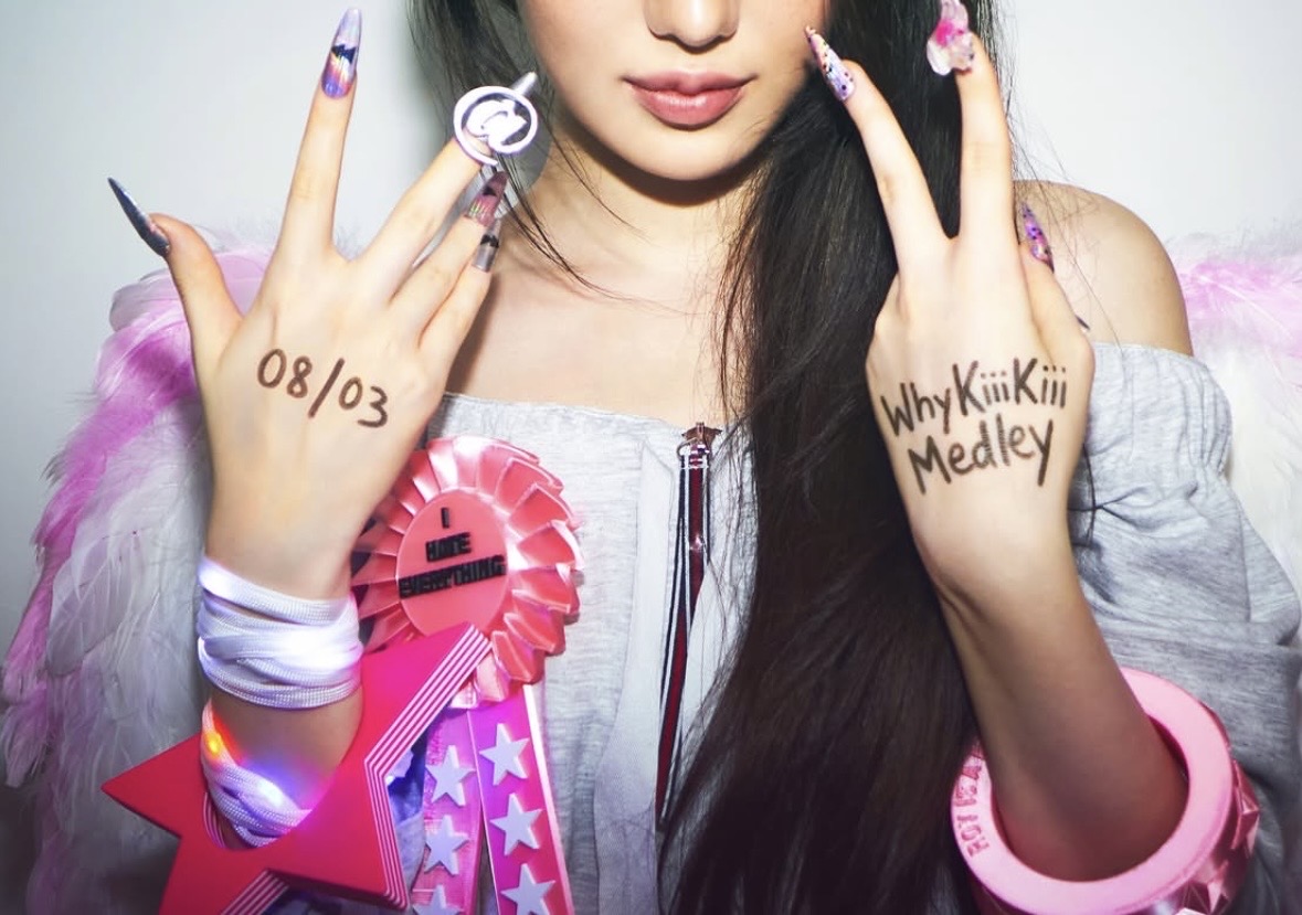 Close-up of a model holding up hands with handwritten lettering, a pink rosette and wide pink wrist accessories.