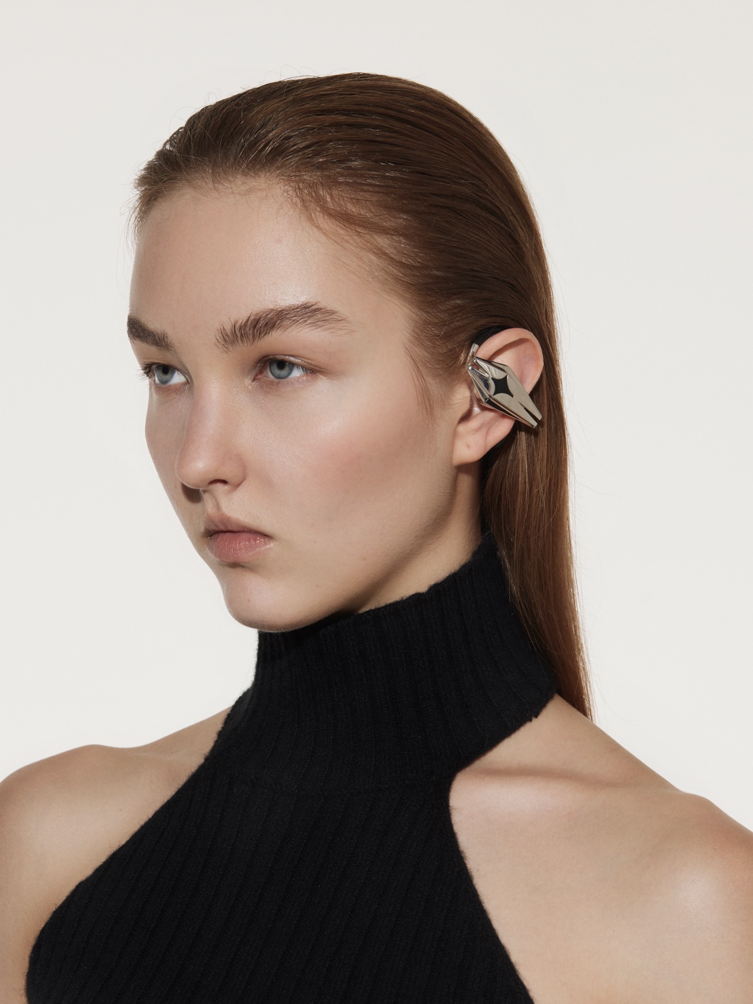 Model wearing an angular silver OF HUNGER STARSHIP earphone with a black sleeveless turtleneck.