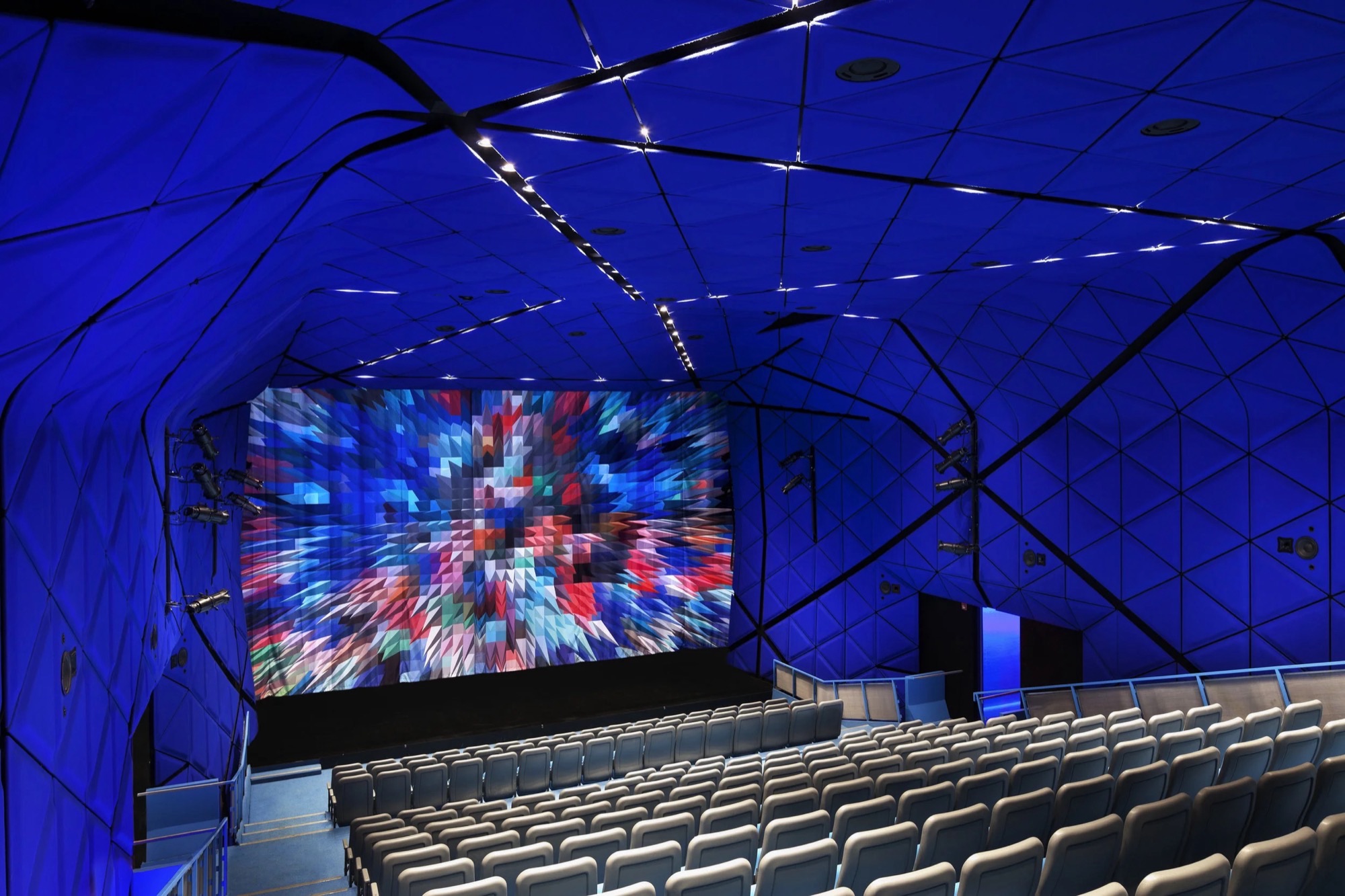 Blue faceted walls and ceiling surround tiered seating and a projection screen at the Museum of the Moving Image.
