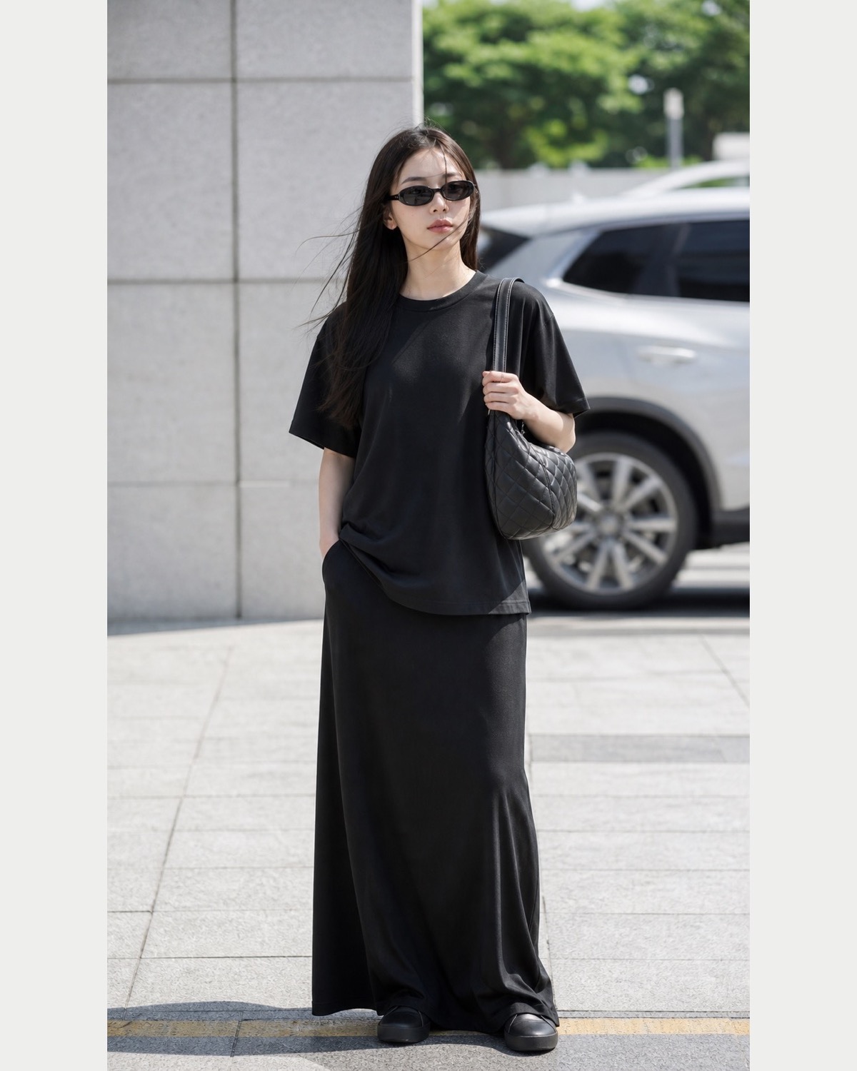 Plain oversized black T-shirt and long fluid black skirt with a simple quilted bag